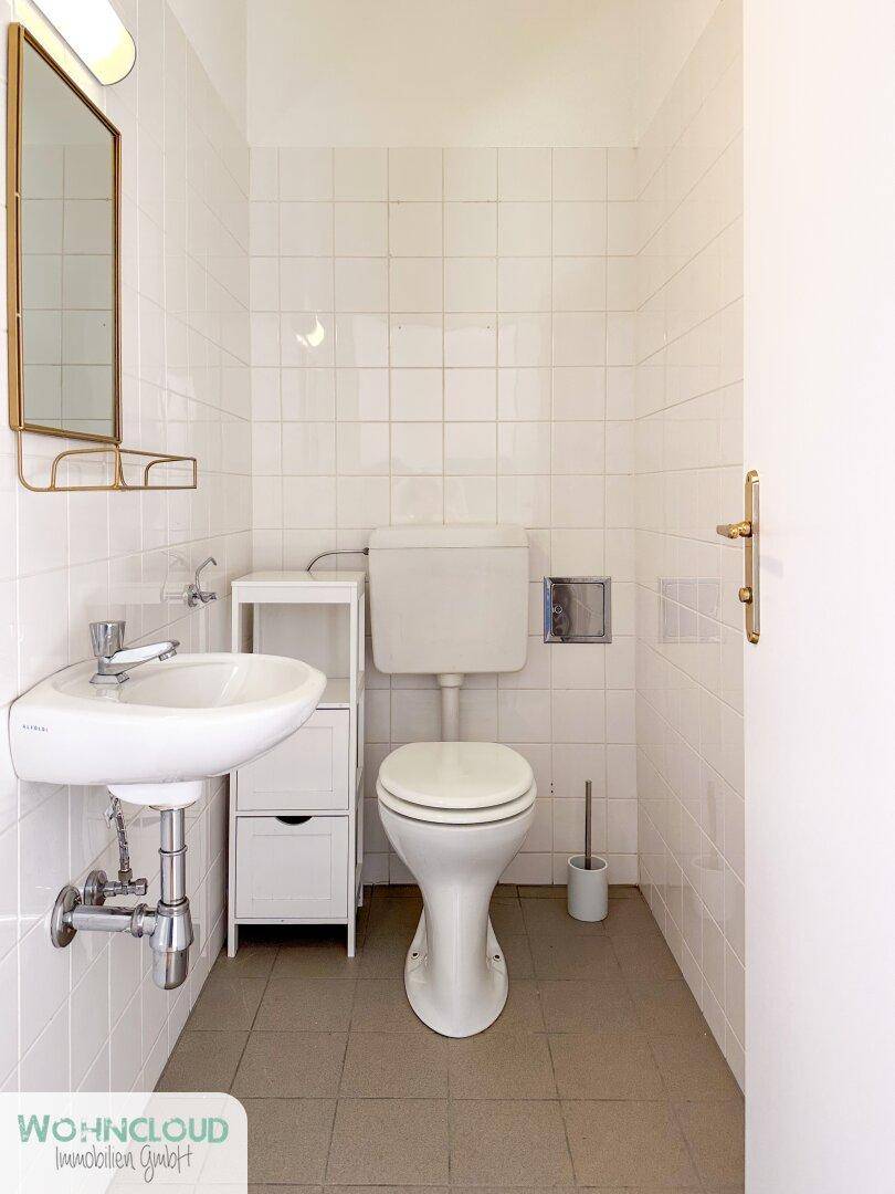 Kleines Gäste-WC mit weißen Wandfliesen, Toilette und Handwaschbecken.