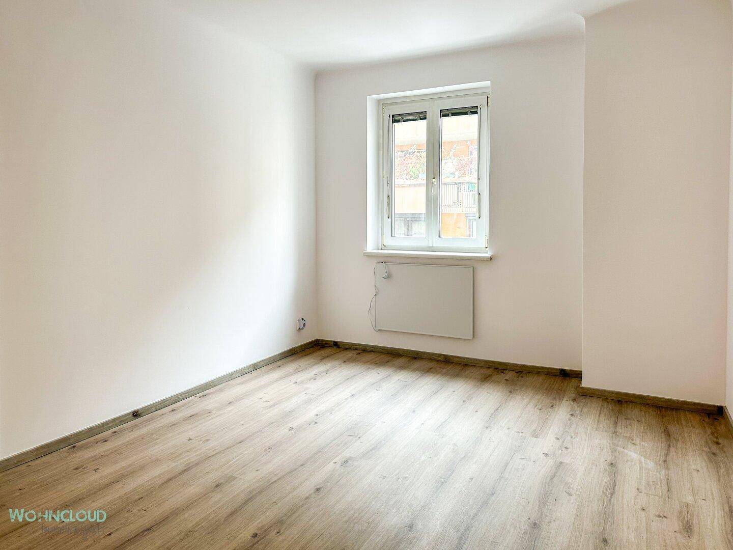 Helles, leeres Zimmer mit Holzboden und Fenster, bereit für neue Bewohner.
