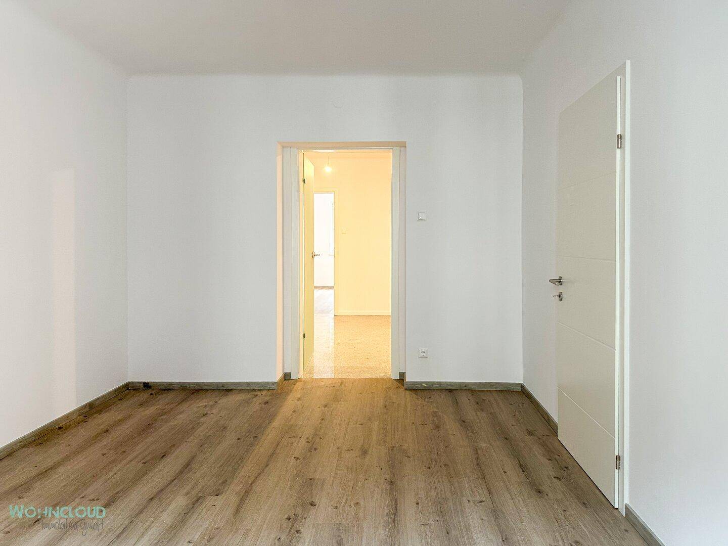 Leeres Zimmer mit Holzboden und offener Tür, bietet vielseitige Nutzungsmöglichkeiten.