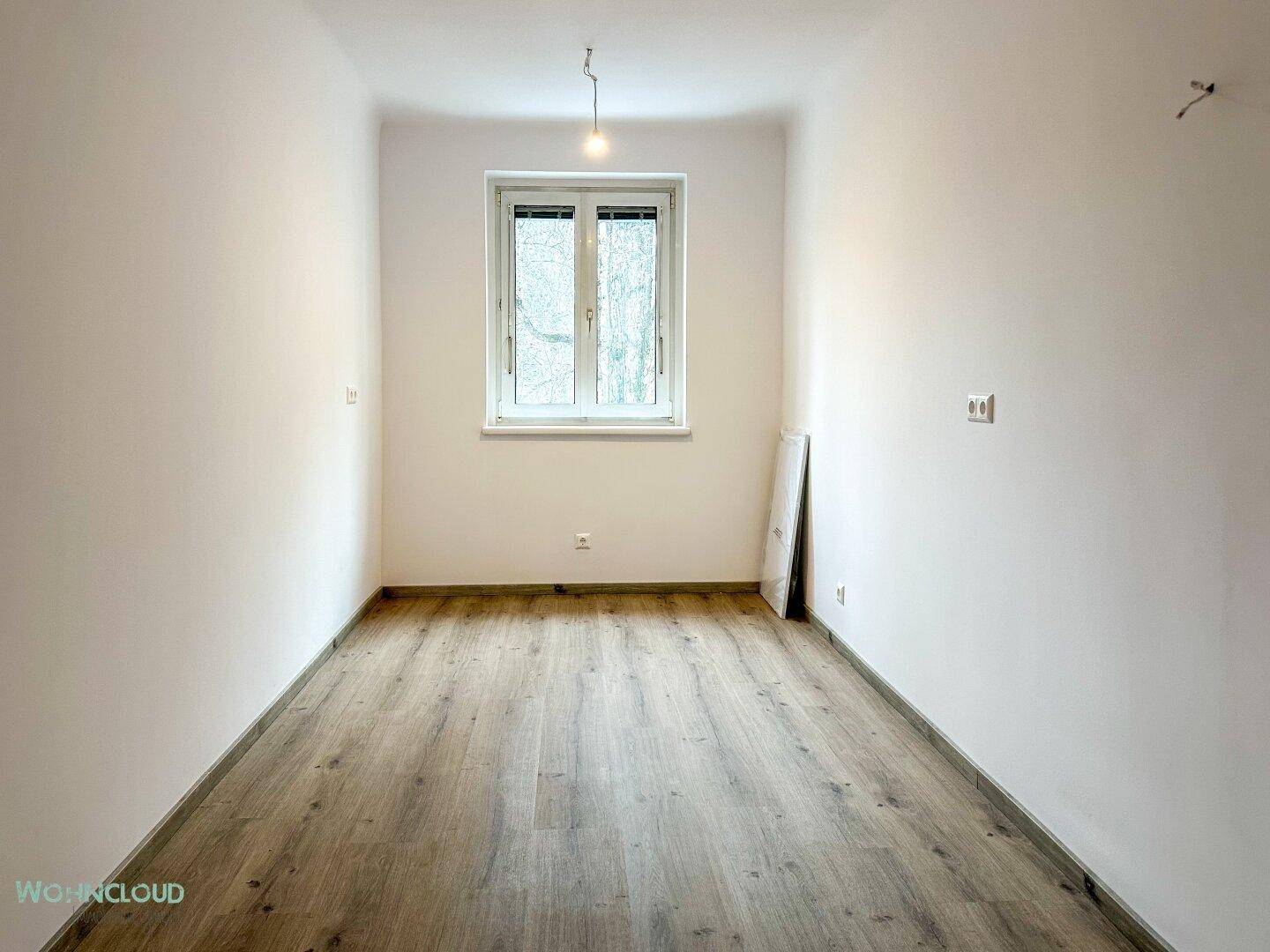 Leeres Zimmer mit Holzboden und Fenster, ideal als Schlaf- oder Arbeitszimmer.