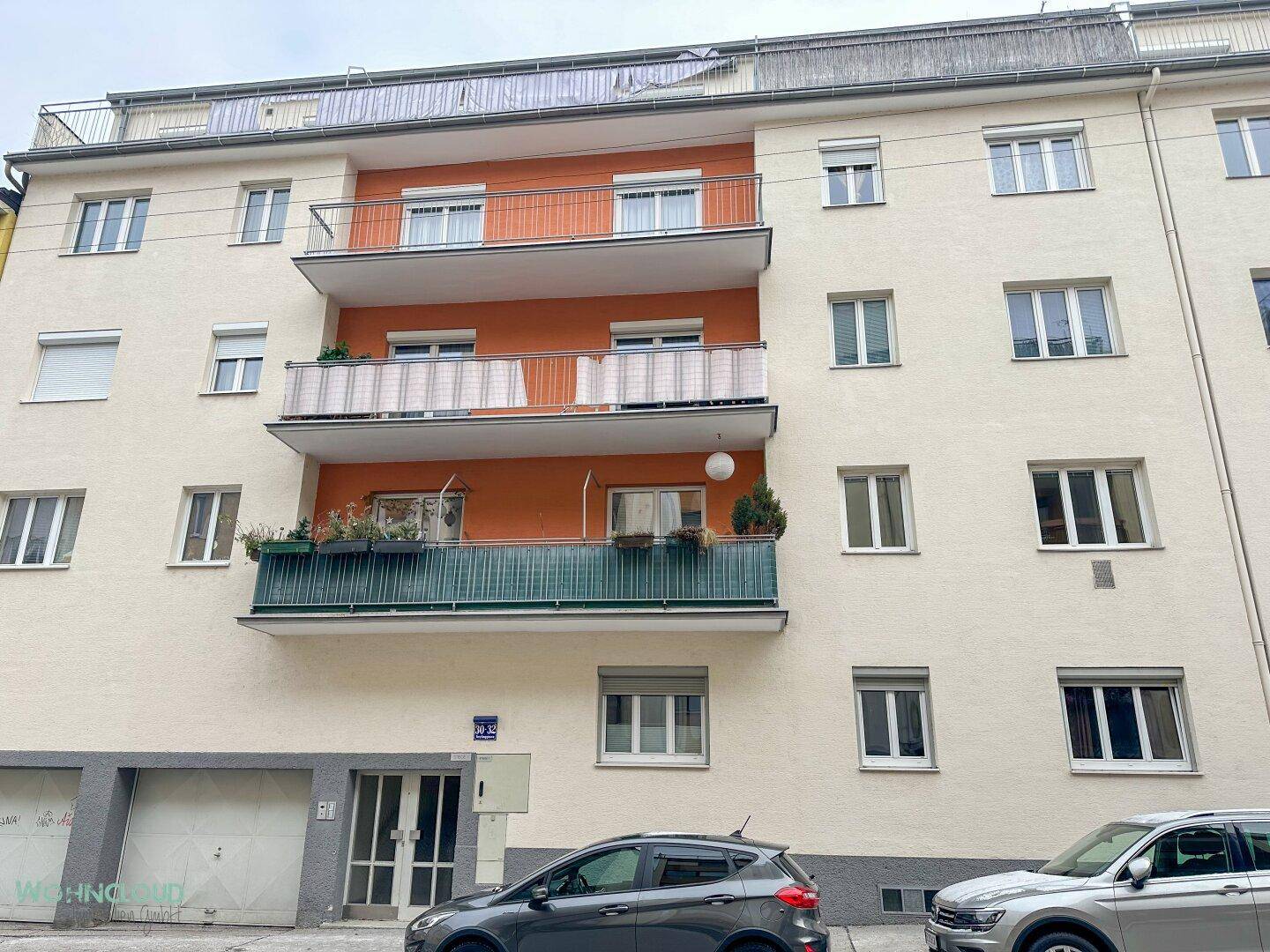 Mehrfamilienhaus mit beiger Fassade, orangefarbenen Balkonen und großen Fenstern.