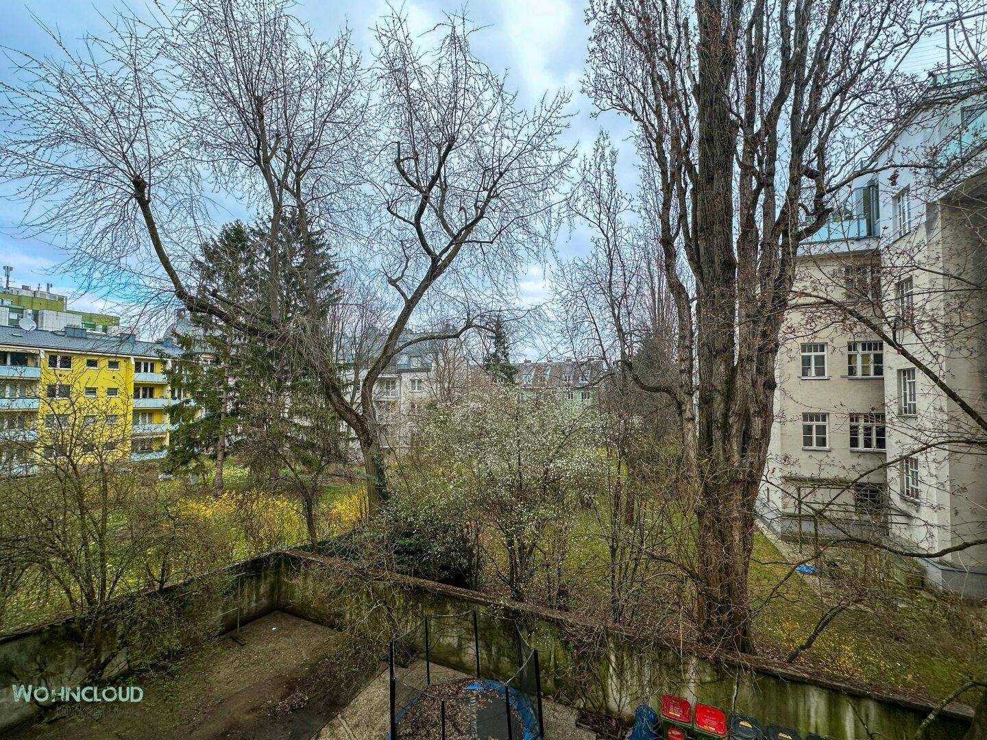 Blick aus dem Fenster auf einen begrünten Innenhof mit Bäumen und umliegenden Gebäuden.