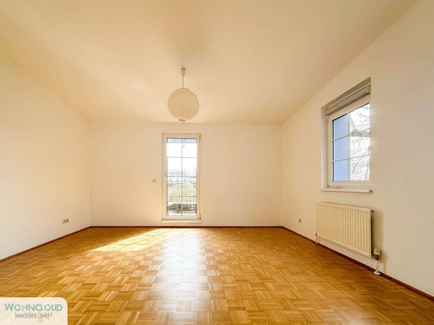 Heller, leerer Raum mit Fischgrätparkett und Zugang zu einem kleinen Balkon.