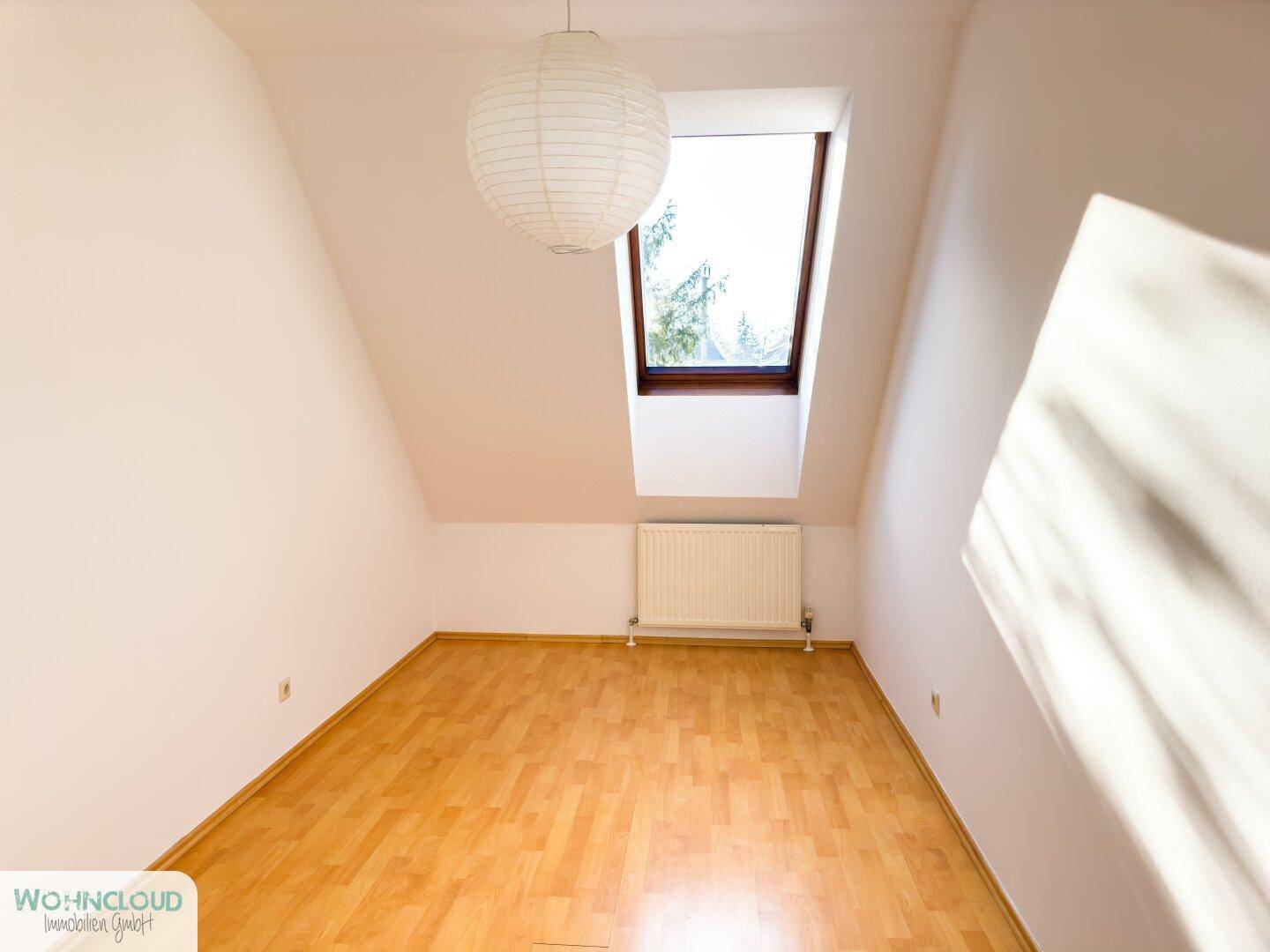 Gemütliches Dachzimmer mit schrägen Wänden, Parkettboden und einem Dachfenster.