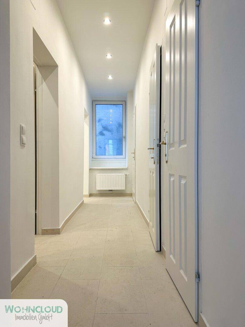 Heller Flur mit Fliesenboden und Einbaustrahlern, der zu weiteren Räumen in der Wohnung führt.