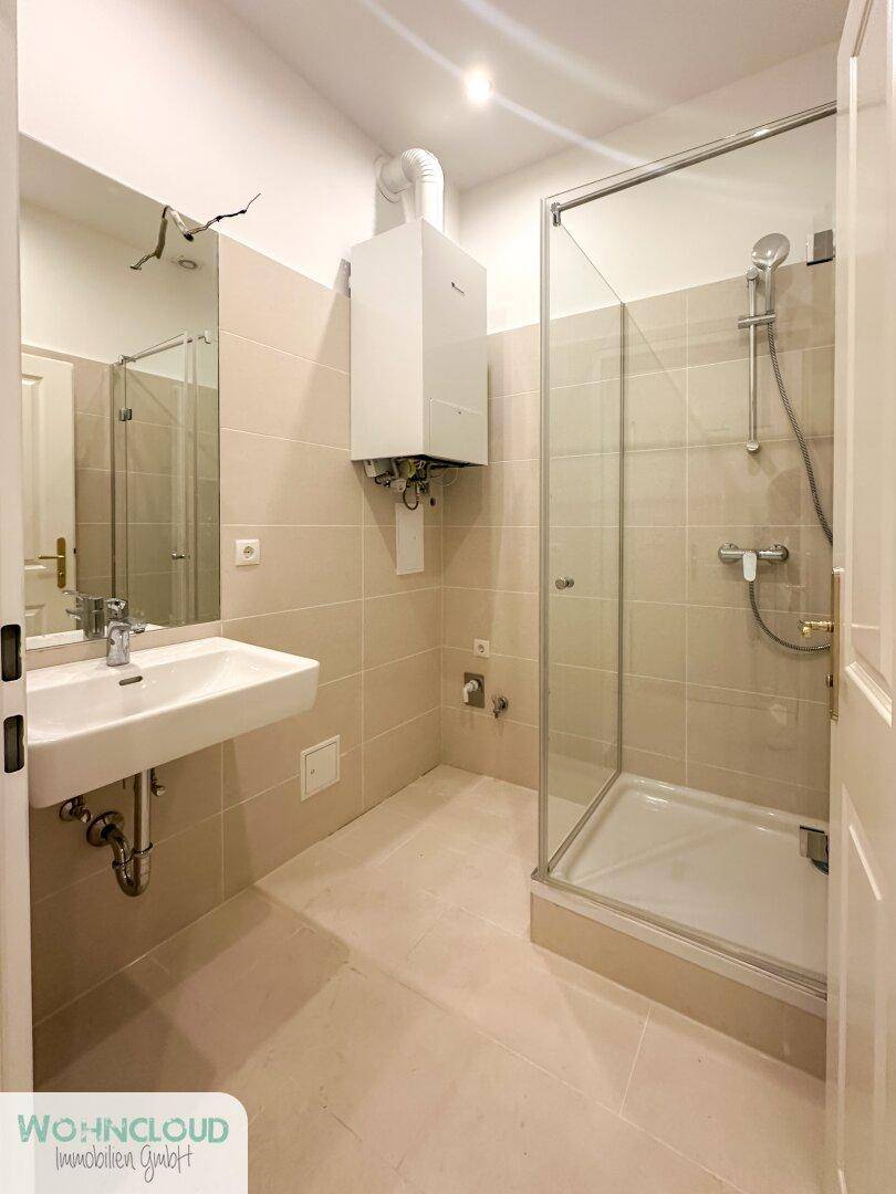 Modernes Badezimmer mit Duschkabine, Waschbecken und beigen Fliesen, inklusive Warmwasserbereiter.