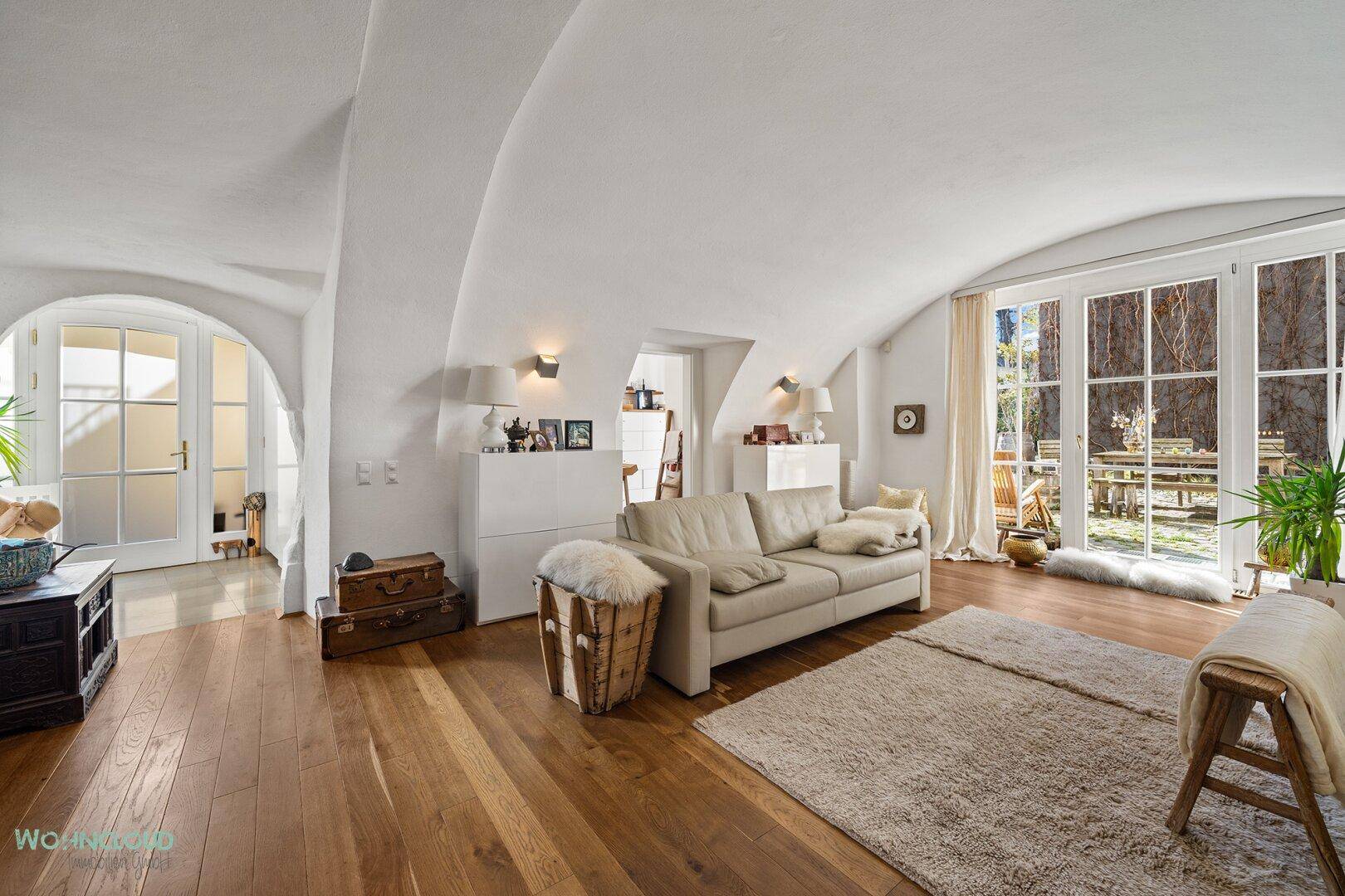 Geräumiges Wohnzimmer mit gewölbter Decke, Holzboden und Zugang zu einem sonnigen Außenbereich.