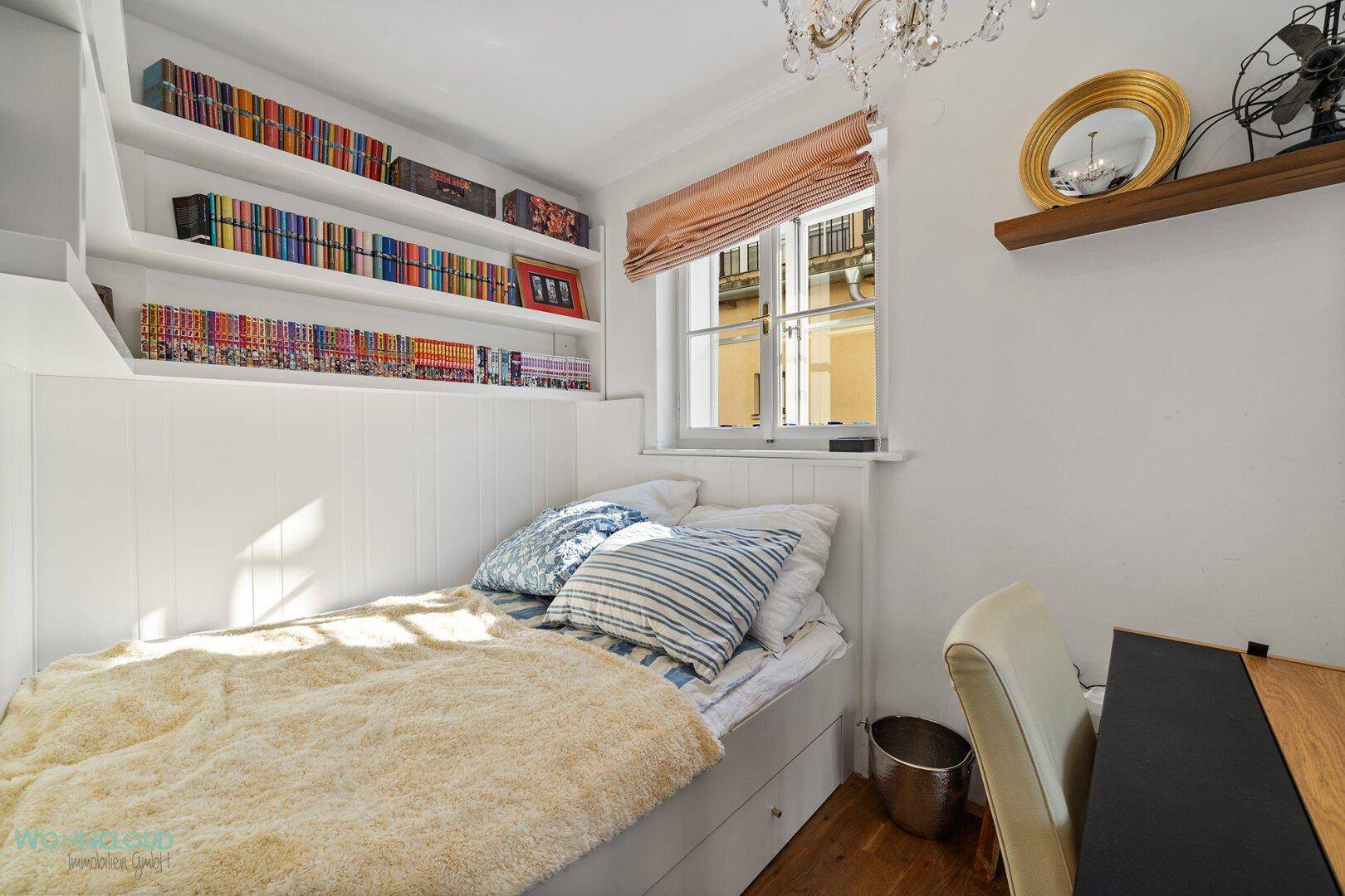 Kleines Schlafzimmer mit integriertem Bett, Schreibtisch und Bücherregalen unter dem Fenster.