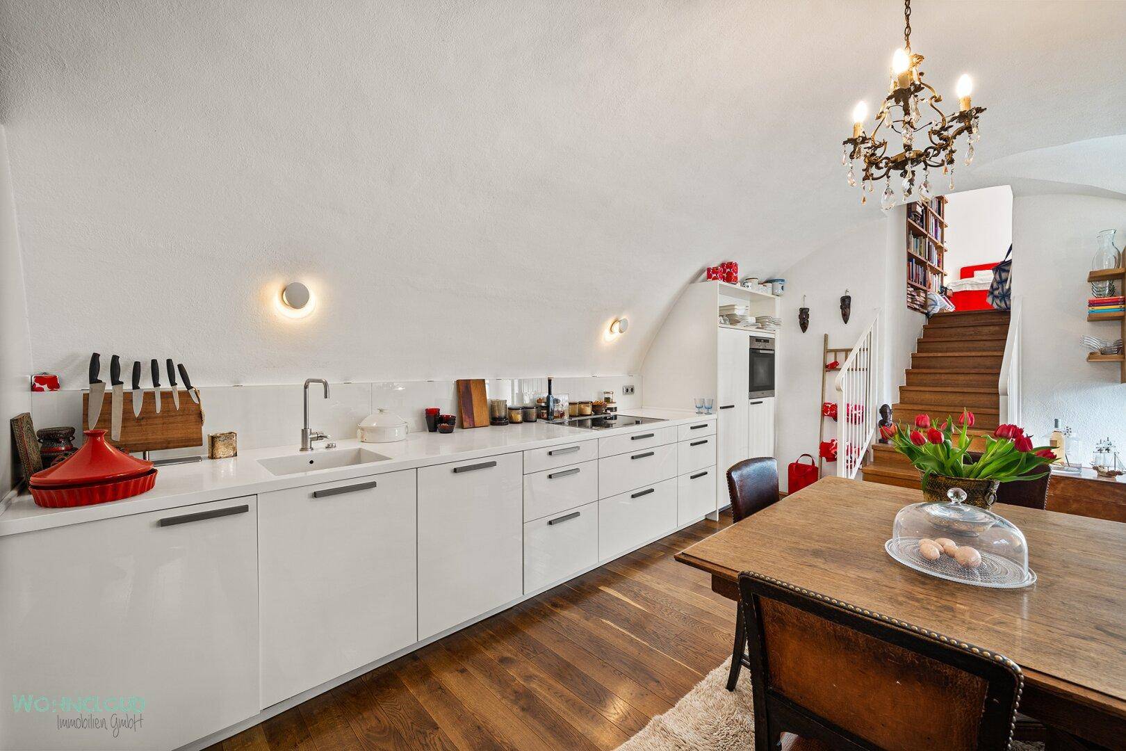 Moderne Küche mit weißen Schränken, Holzboden und Essbereich unter einer Dachschräge.
