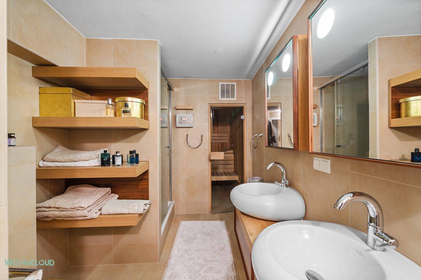 Geräumiges Badezimmer mit Doppelwaschbecken, Holzregalen und direktem Zugang zur Sauna.