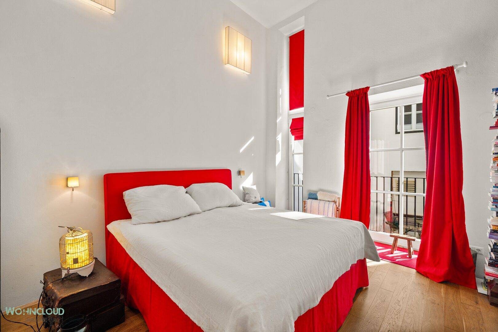 Helles Schlafzimmer mit Doppelbett, roten Akzenten und Zugang zu einem französischen Balkon.
