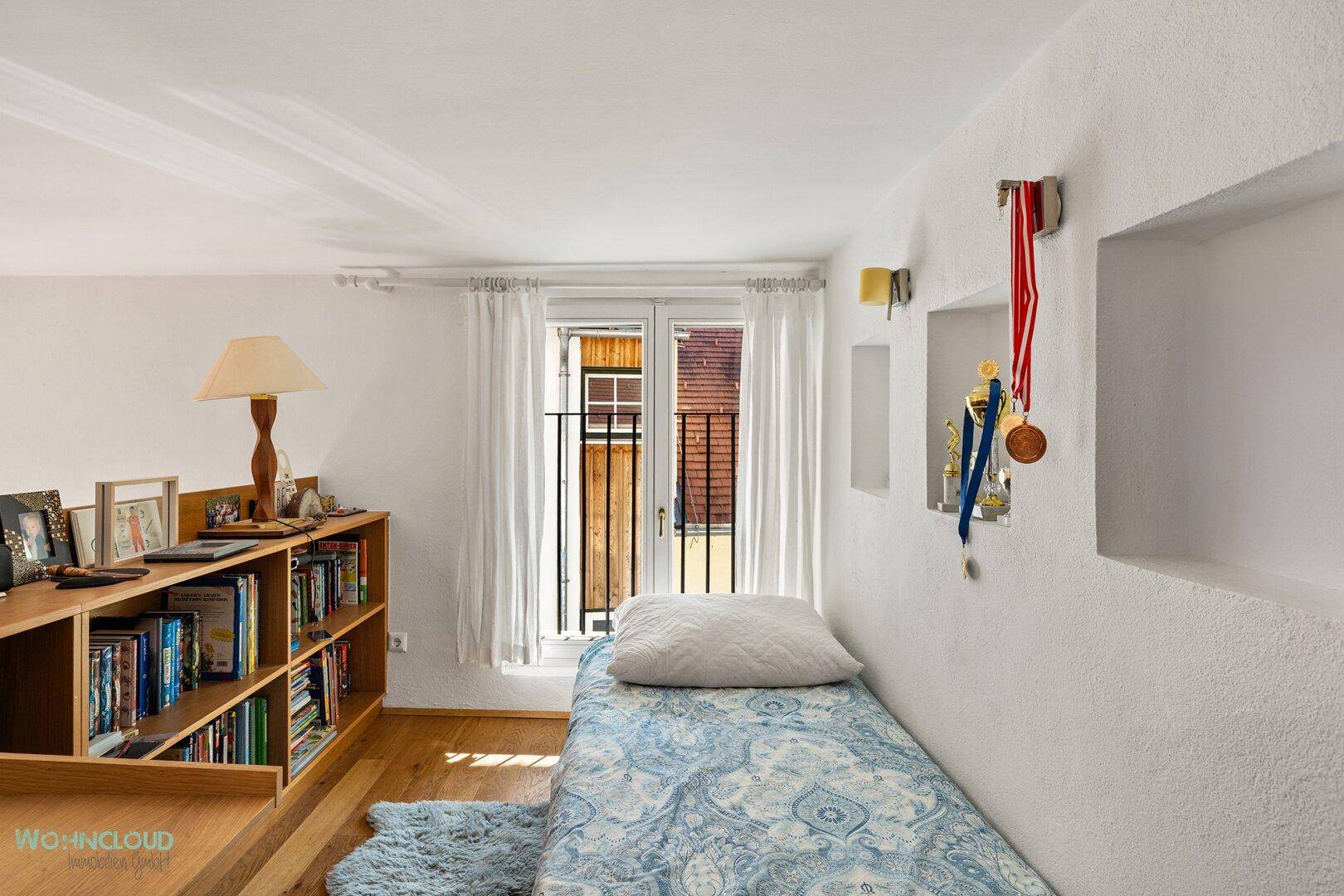 Gemütliches Schlafzimmer mit Holzboden, Bücherregal und Zugang zu einem französischen Balkon.