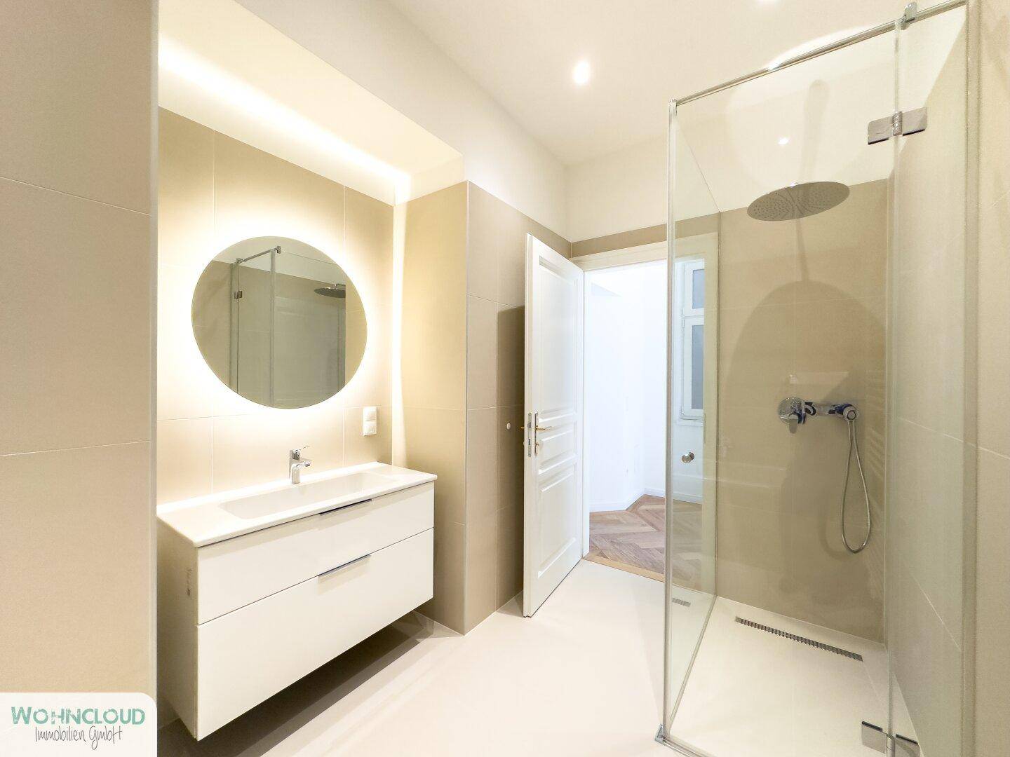Modernes Badezimmer mit schwebendem Waschtisch, beleuchtetem Spiegel und geräumiger Duschkabine.