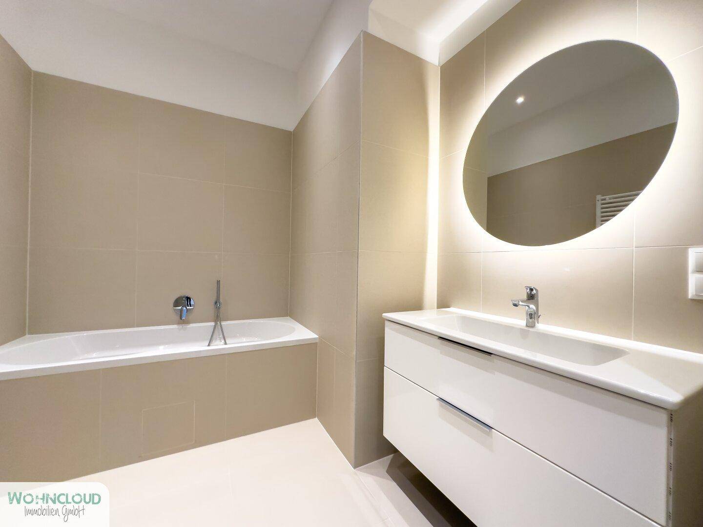 Elegantes Badezimmer mit integrierter Badewanne, modernem Waschtisch und beleuchtetem Wandspiegel.