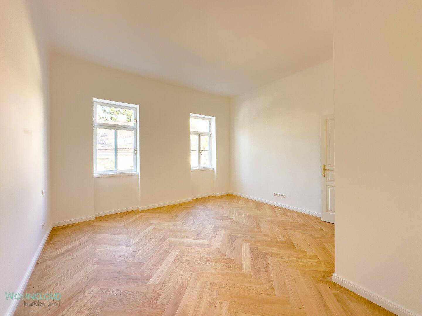 Geräumiges Schlafzimmer mit elegantem Fischgrätparkett und weiß gestrichenen Wänden, bereit zur individuellen Gestaltung.