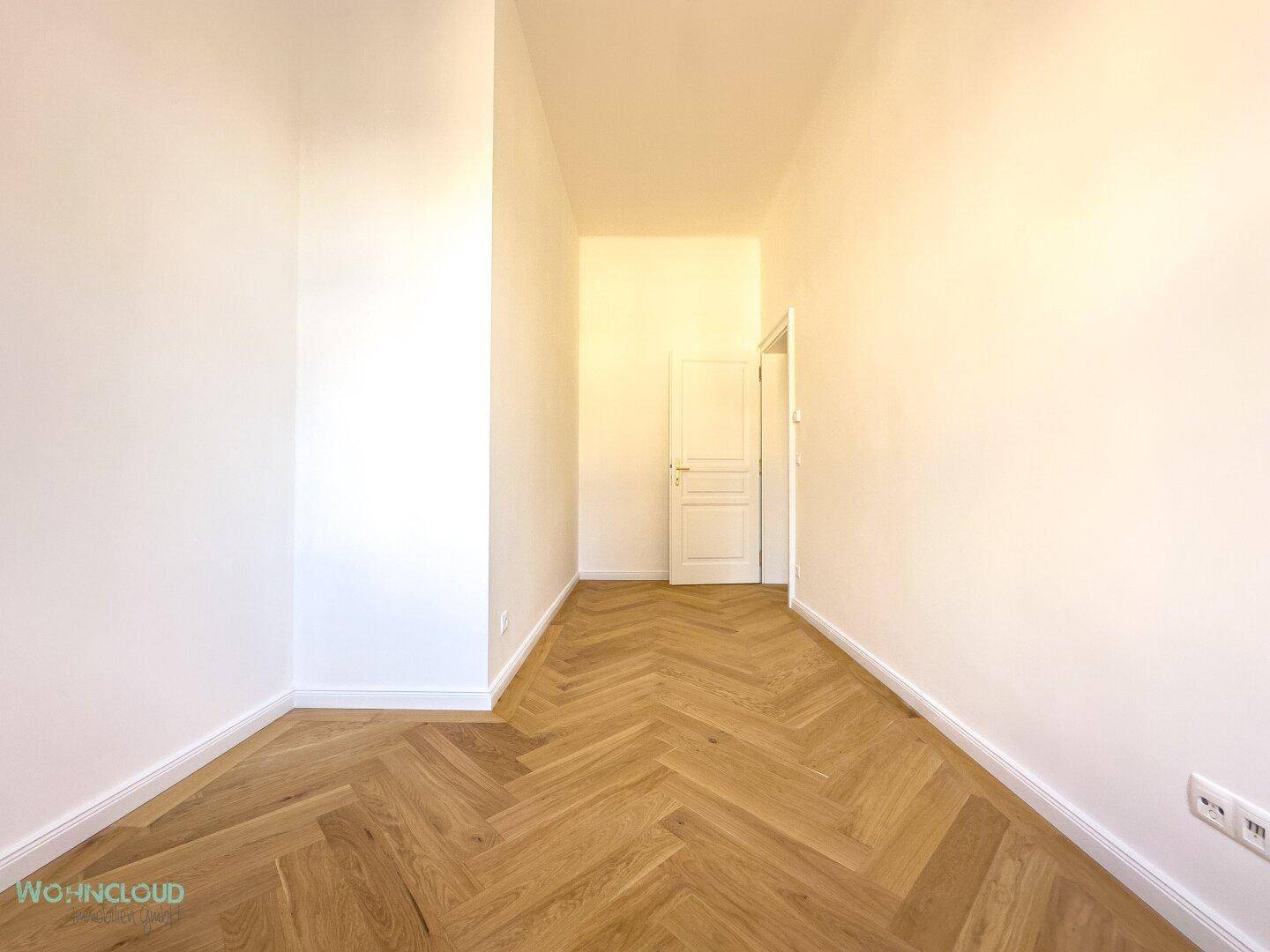 Langer, heller Flur mit elegantem Fischgrätparkett und weißen Wänden, der zu weiteren Räumen führt.