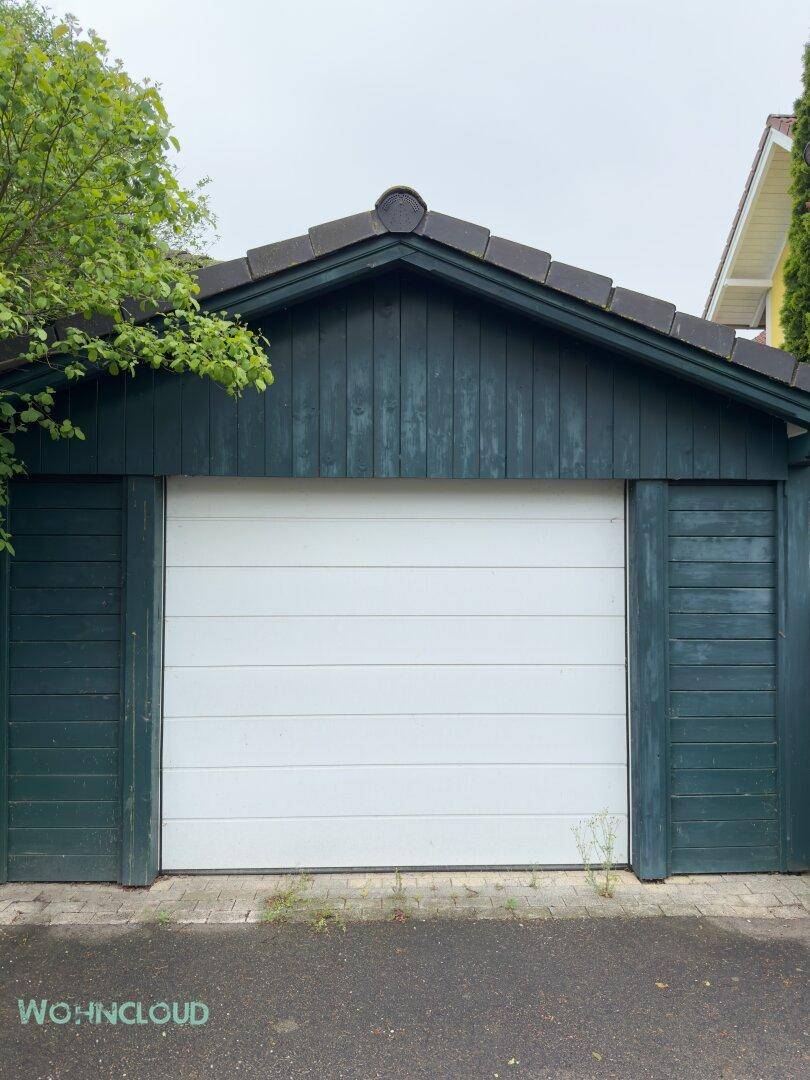 Einzelgarage mit weißem Tor und dunkelgrüner Holzverkleidung.