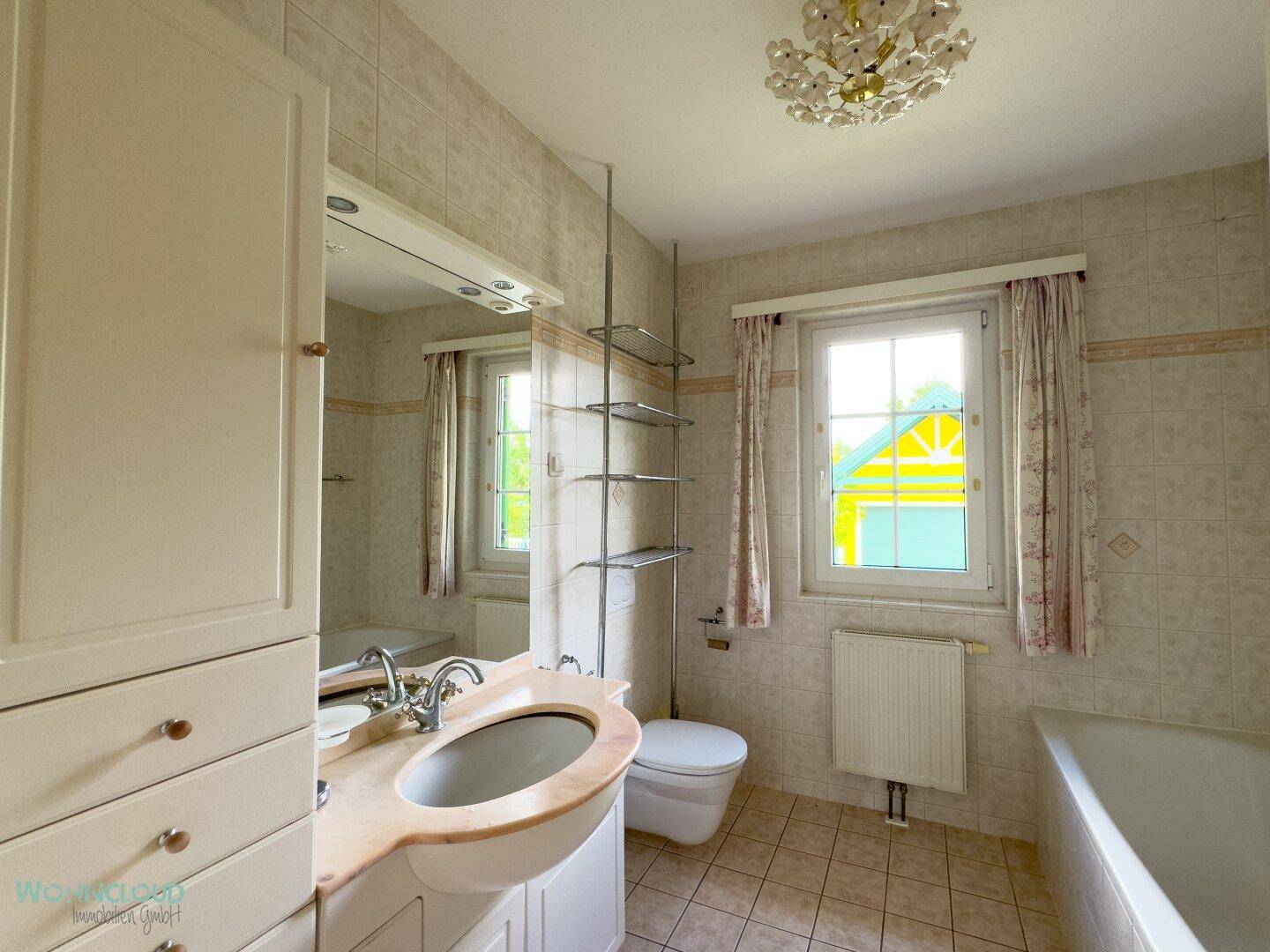 Gefliestes Badezimmer mit Badewanne, Einzelwaschbecken und Fenster für Tageslicht.