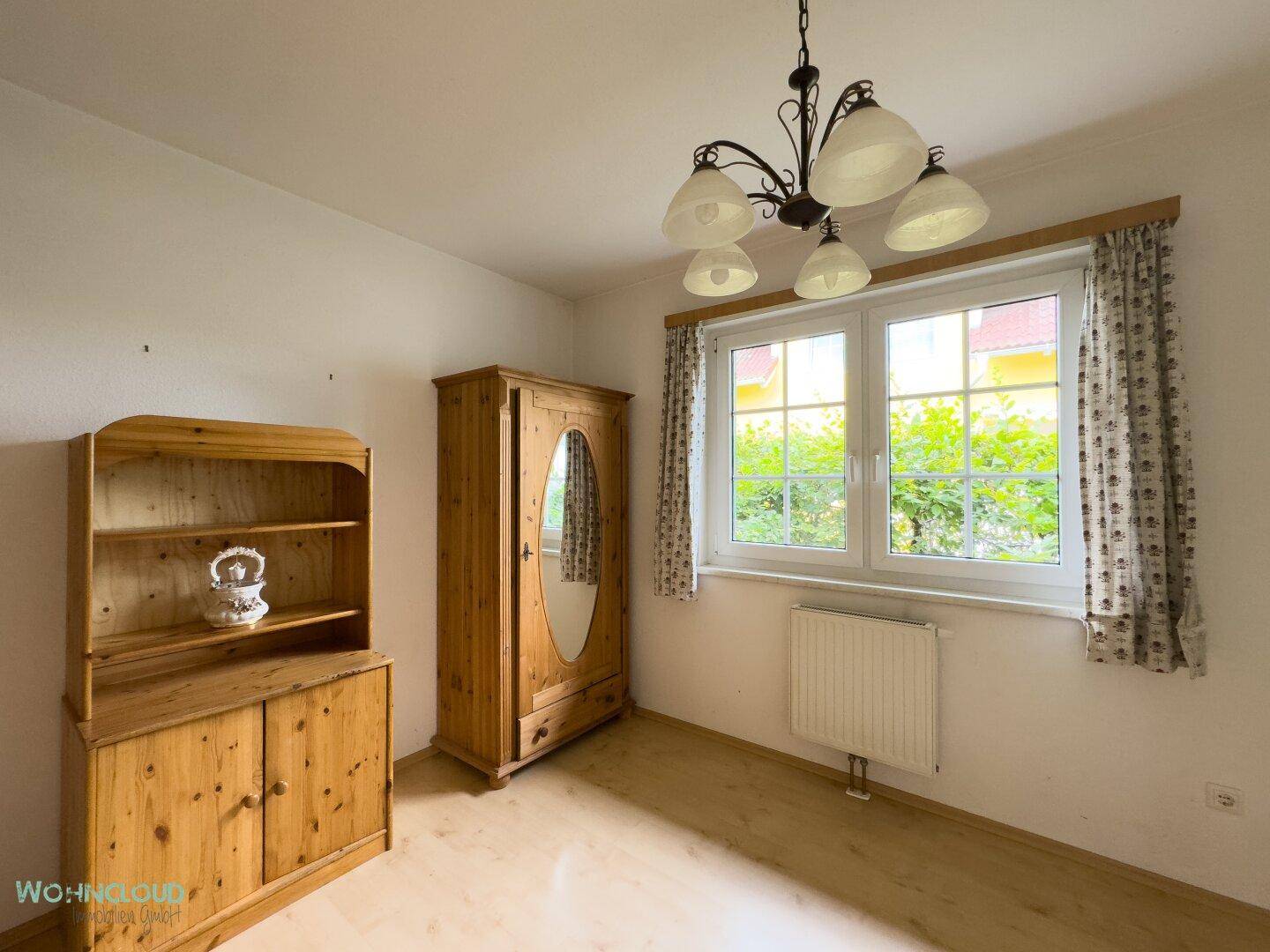Schlafzimmer mit traditionellen Holzmöbeln, Laminatboden und Blick ins Grüne.