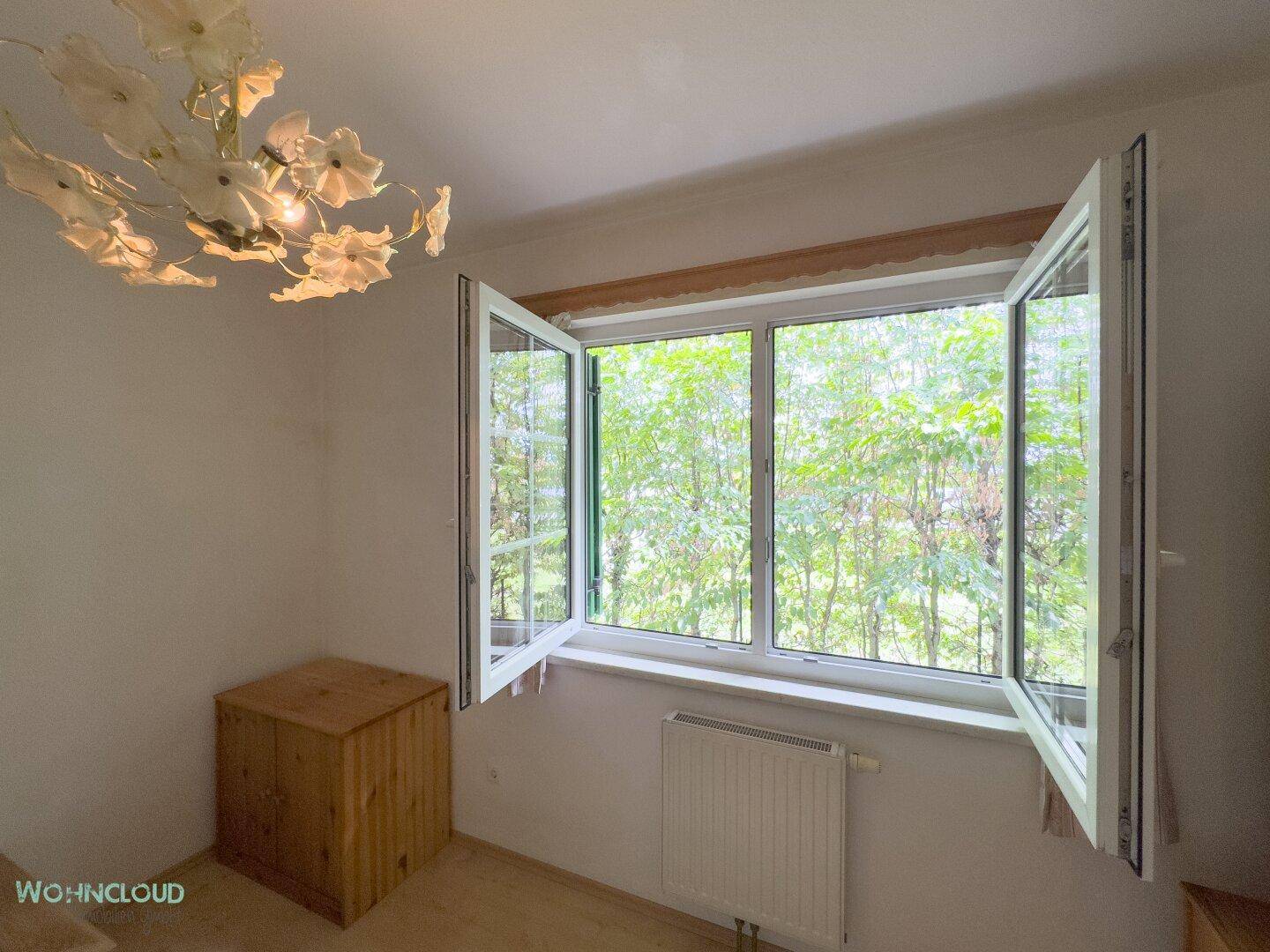 Helles Zimmer mit geöffnetem Fenster, das einen Blick auf üppiges Grün bietet.