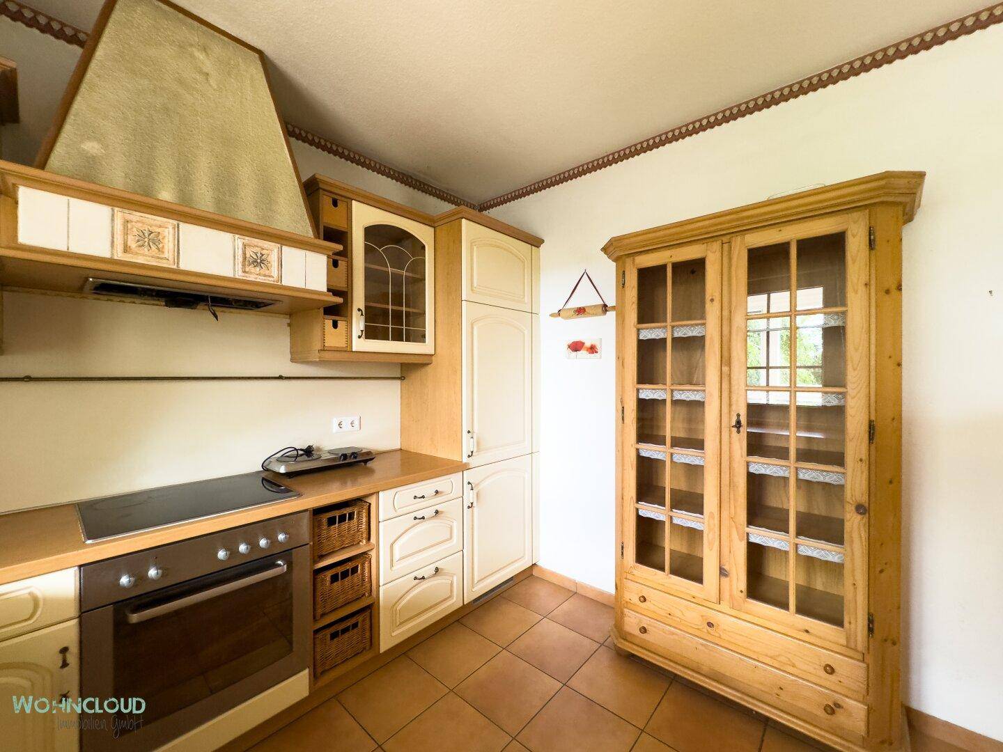 Traditionelle Küche mit hellen Schränken, Holzarbeitsplatte und einem Vitrinenschrank.