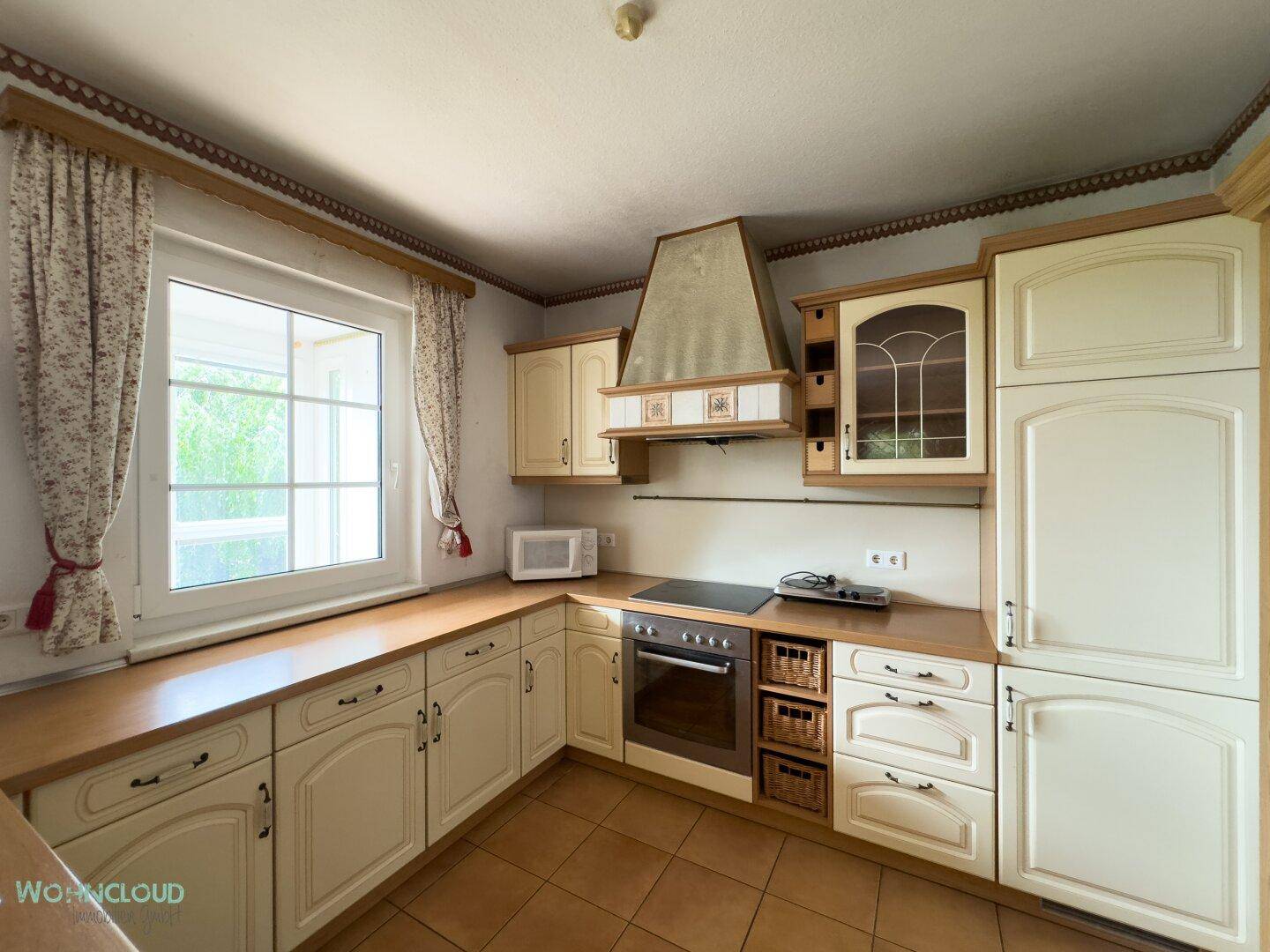 Traditionelle Küche mit hellen Schränken, Holzarbeitsplatte und integrierten Geräten.