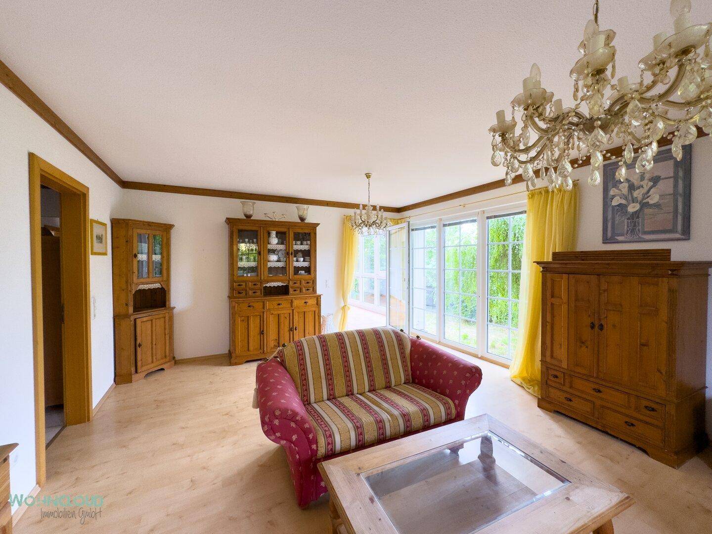 Gemütliches Wohnzimmer mit traditionellen Holzmöbeln, Laminatboden und Zugang zum Garten.