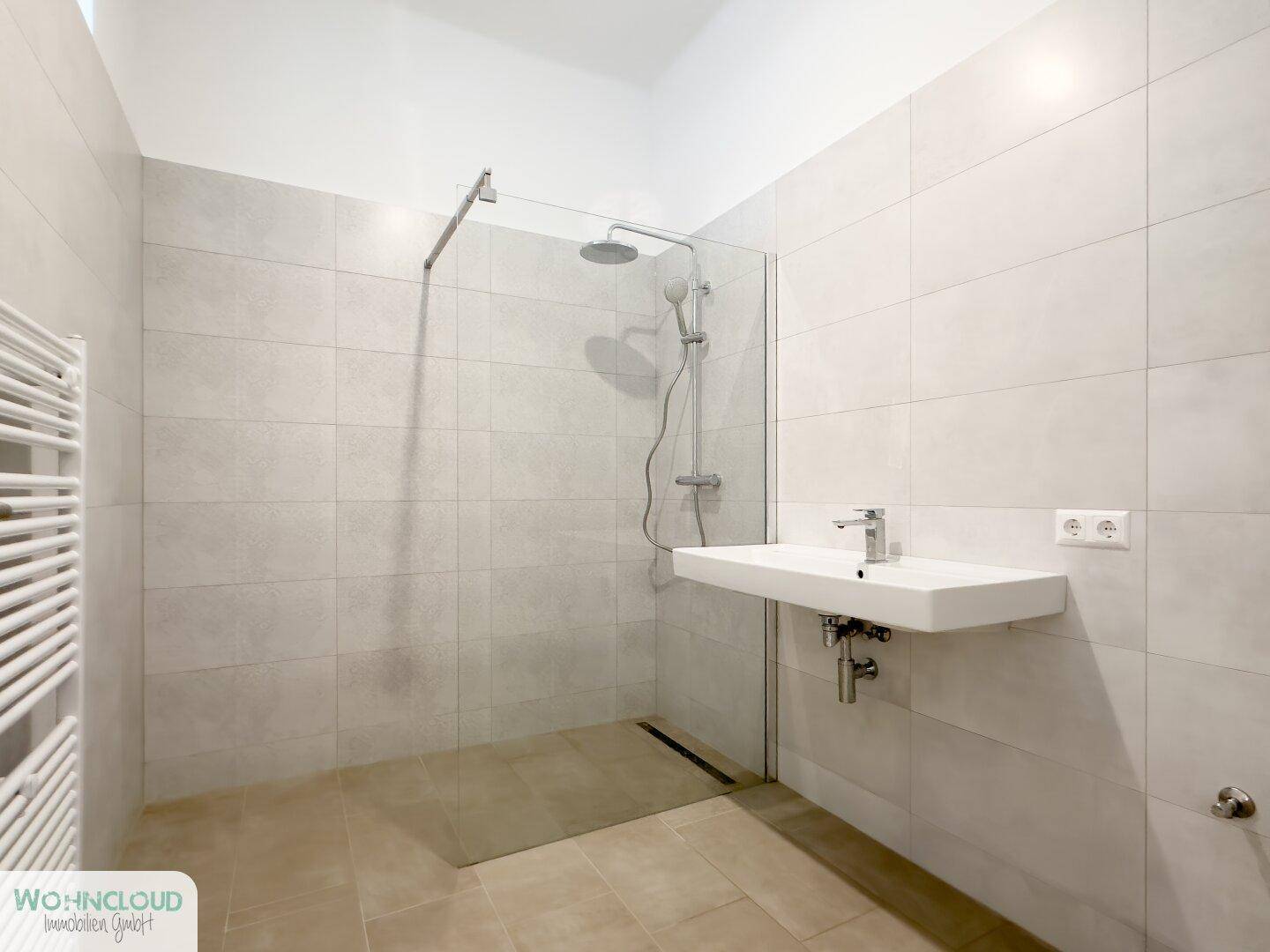 Modernes Badezimmer mit ebenerdiger Dusche, Wandwaschbecken und hellen Fliesen.