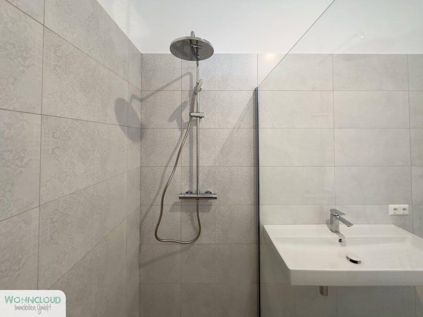 Detaillierte Ansicht der modernen Dusche mit Regenduschkopf und Wandwaschbecken im Badezimmer.