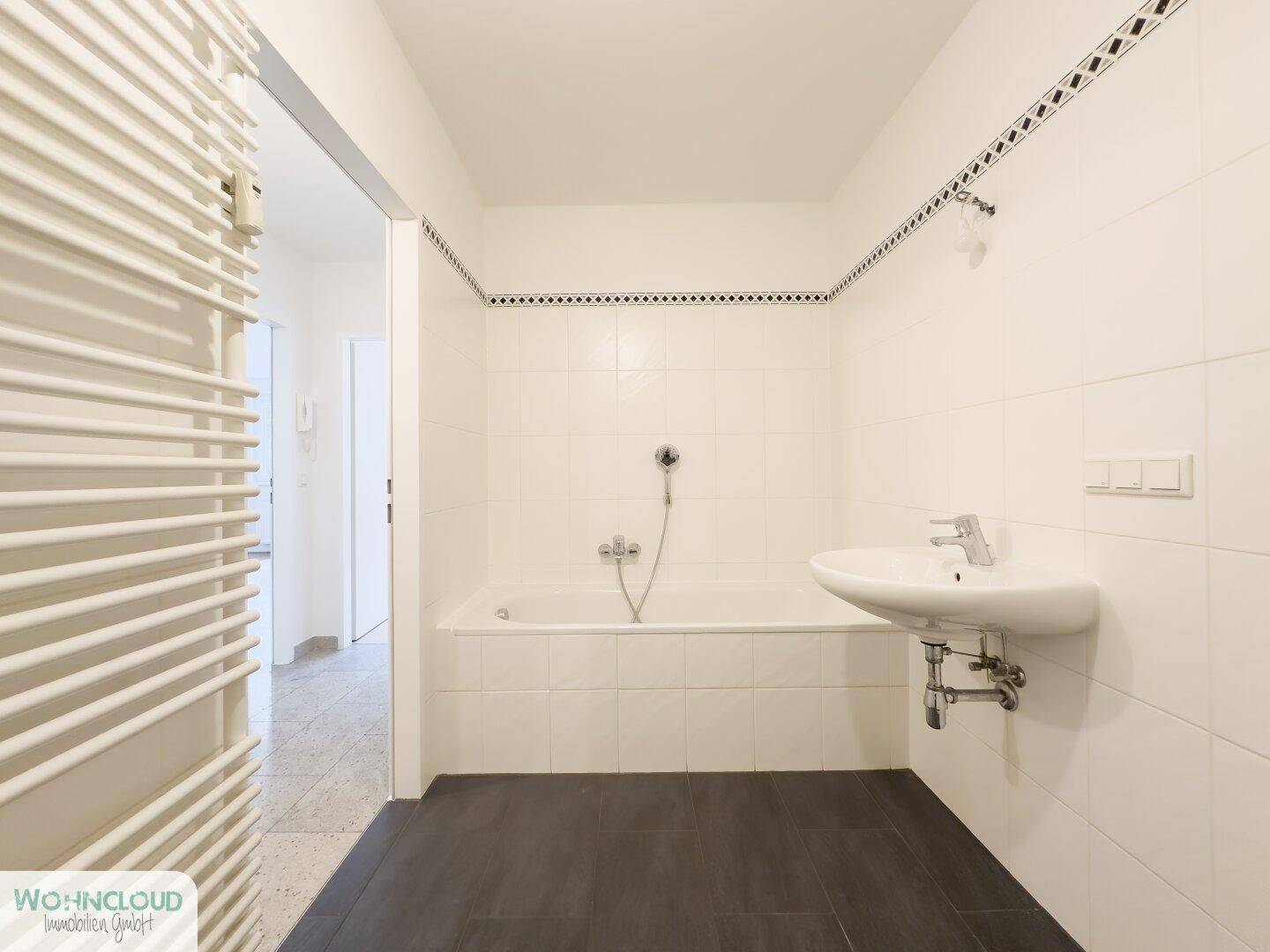 Helles Badezimmer mit Badewanne, Waschbecken und beheiztem Handtuchhalter.