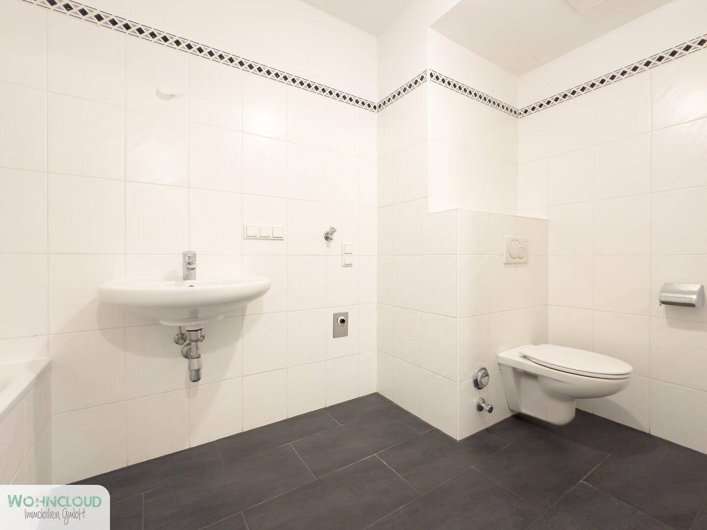 Modern gefliestes Badezimmer mit Waschbecken, Toilette und dunklem Boden.