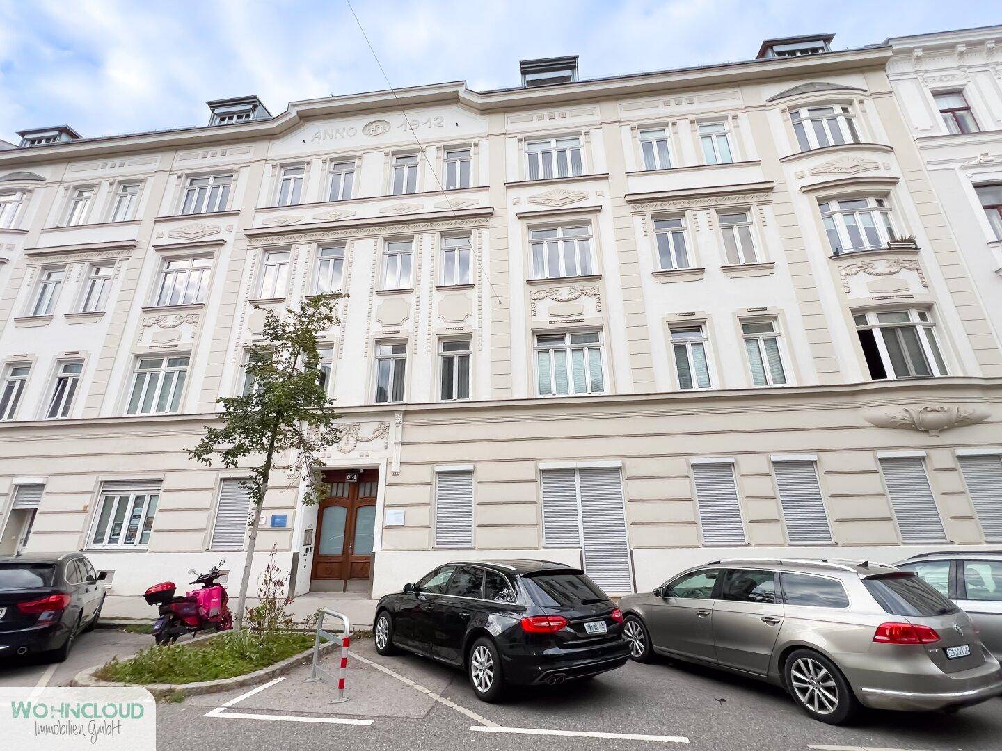 Historisches Mehrfamilienhaus mit klassischer Fassade, vielen Fenstern und Parkplätzen davor.