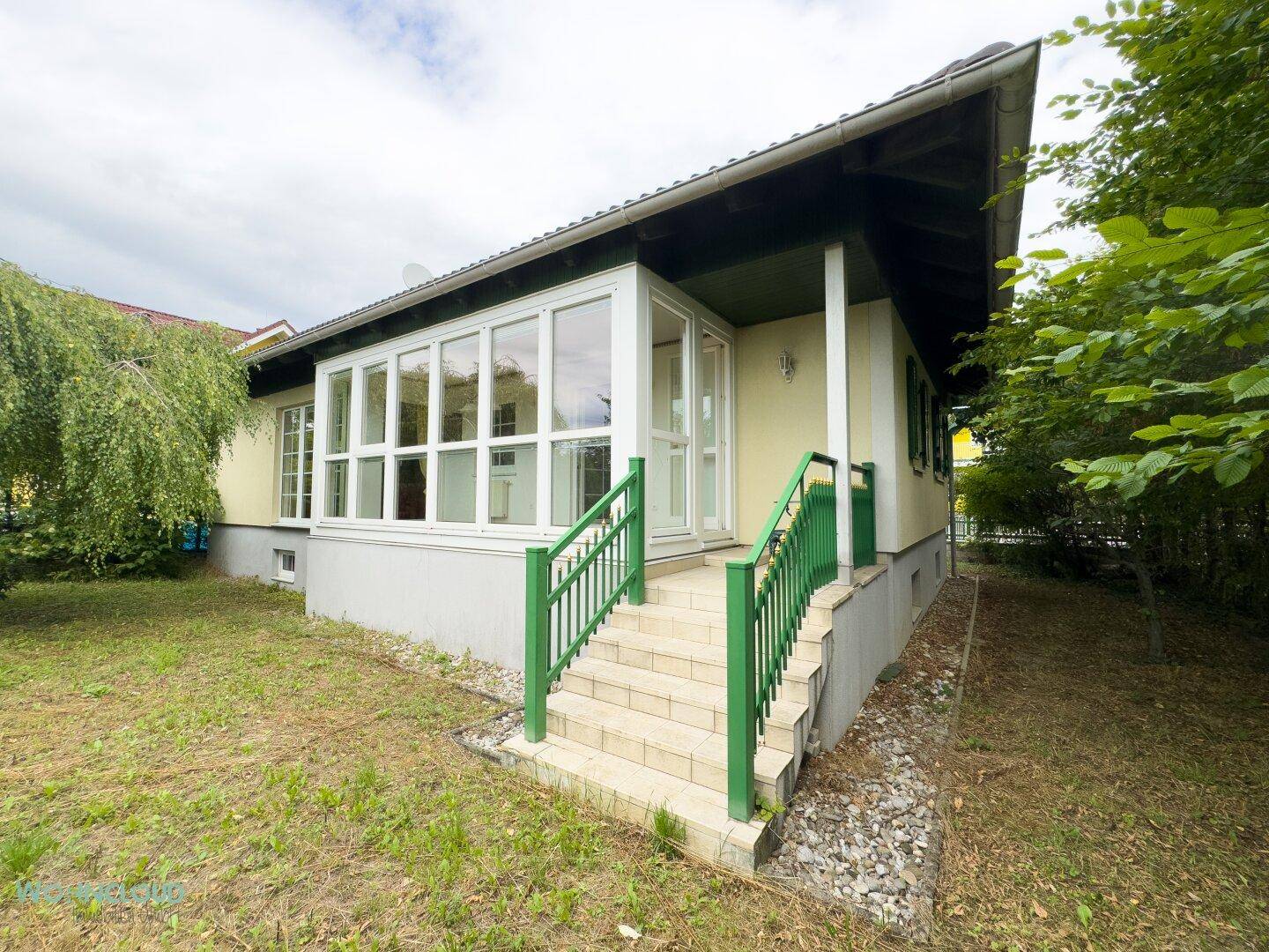 Seitenansicht des Hauses mit Wintergarten und Zugang zum Garten über eine Treppe.
