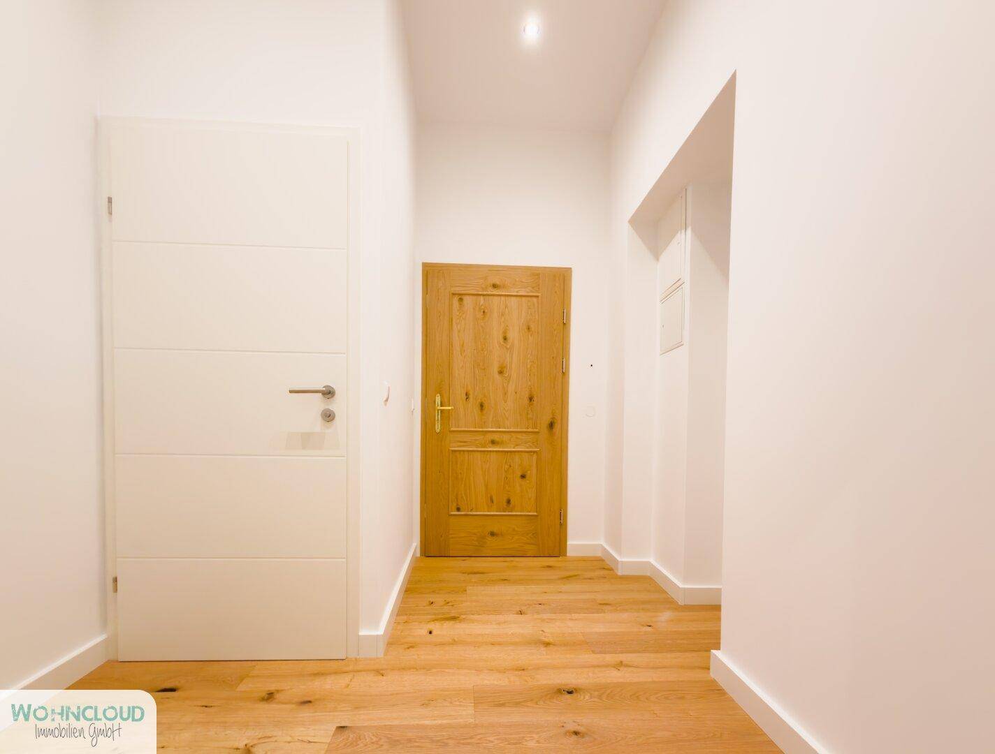 Heller Flur mit Holzboden und zwei Türen, der verschiedene Räume der Wohnung verbindet.