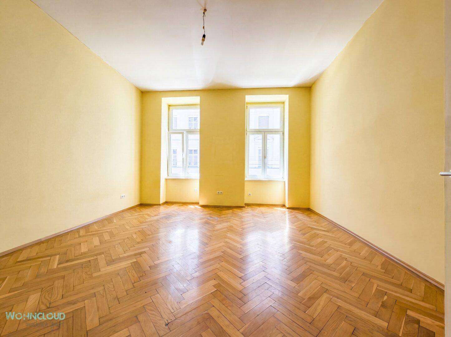 Leeres Zimmer mit gelben Wänden und Fischgrätparkett, bereit für individuelle Gestaltung.