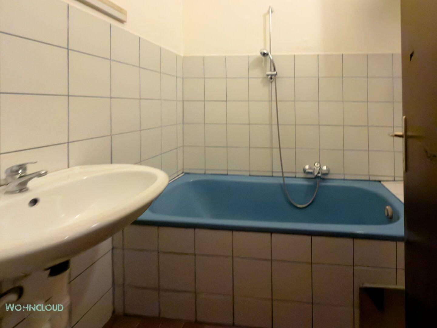 Älteres Badezimmer mit blauer Badewanne, weiß-blauen Fliesen und Waschbecken.
