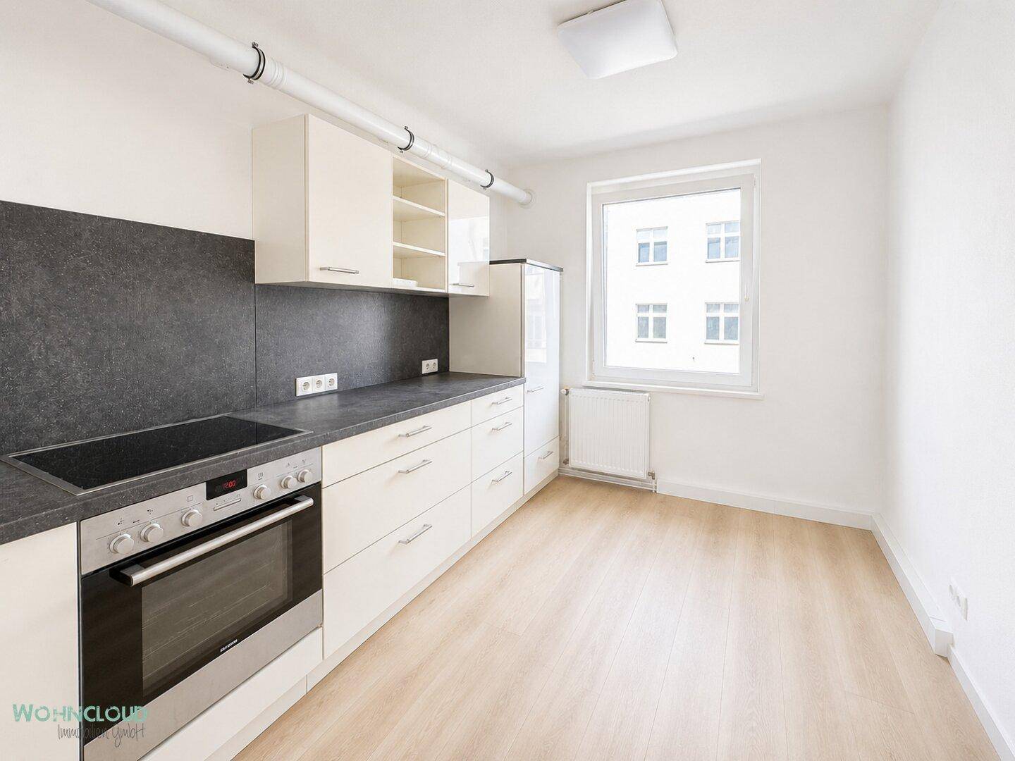 Funktionale Küche mit weißen Schränken, dunkler Arbeitsplatte und Fenster.