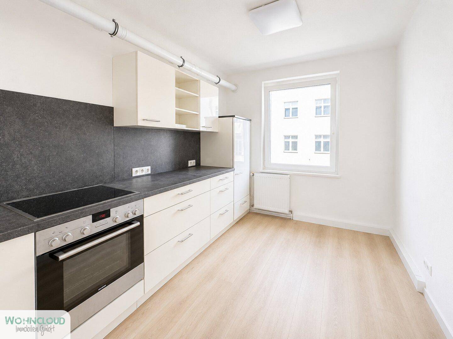 Funktionale Küche mit weißen Schränken, dunkler Arbeitsplatte und integriertem Herd mit Backofen.