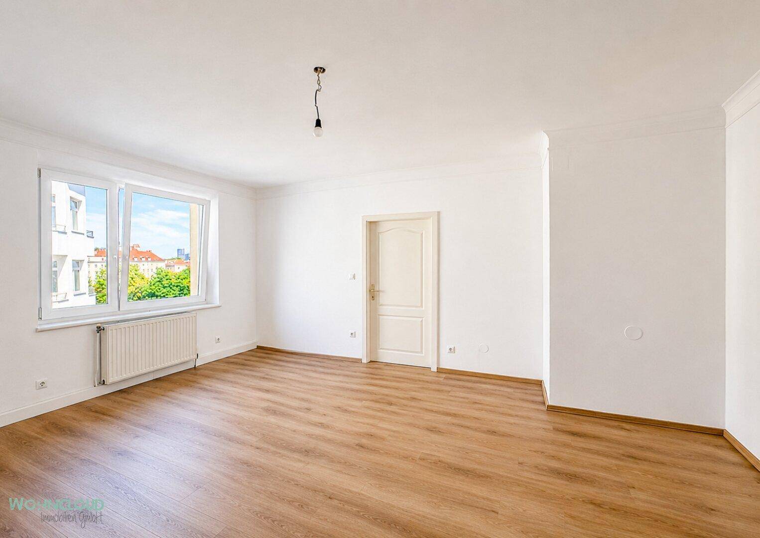 Geräumiges, unmöbliertes Zimmer mit großen Fenstern und hellem Laminatboden.