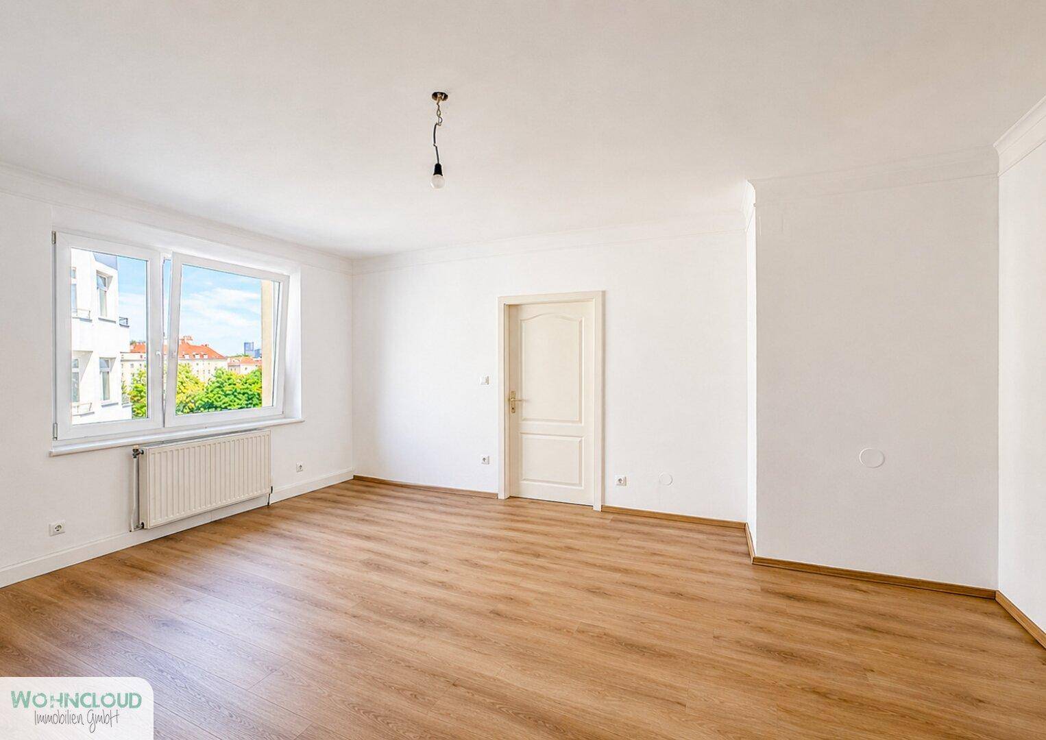Geräumiges, unmöbliertes Wohnzimmer mit großen Fenstern und hellem Laminatboden.