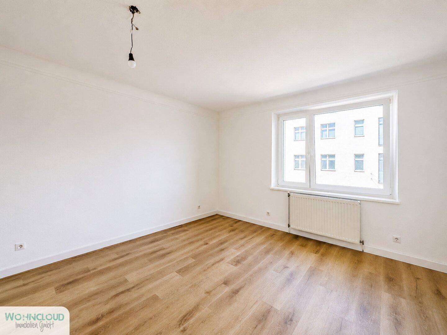 Unmöbliertes Schlafzimmer mit Laminatboden und Fenster, das viel natürliches Licht hereinlässt.