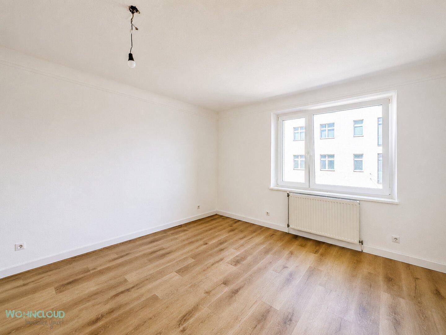 Unmöbliertes Schlafzimmer mit Laminatboden und einem Fenster, das viel Tageslicht hereinlässt.
