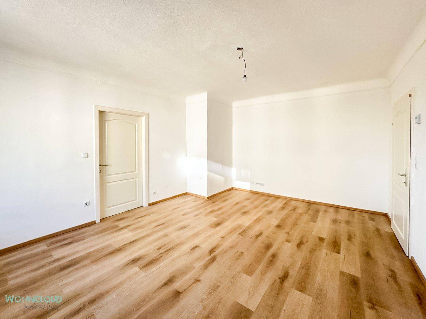 Leeres Zimmer mit hellem Laminatboden und weiß gestrichenen Wänden, bereit zur individuellen Gestaltung.