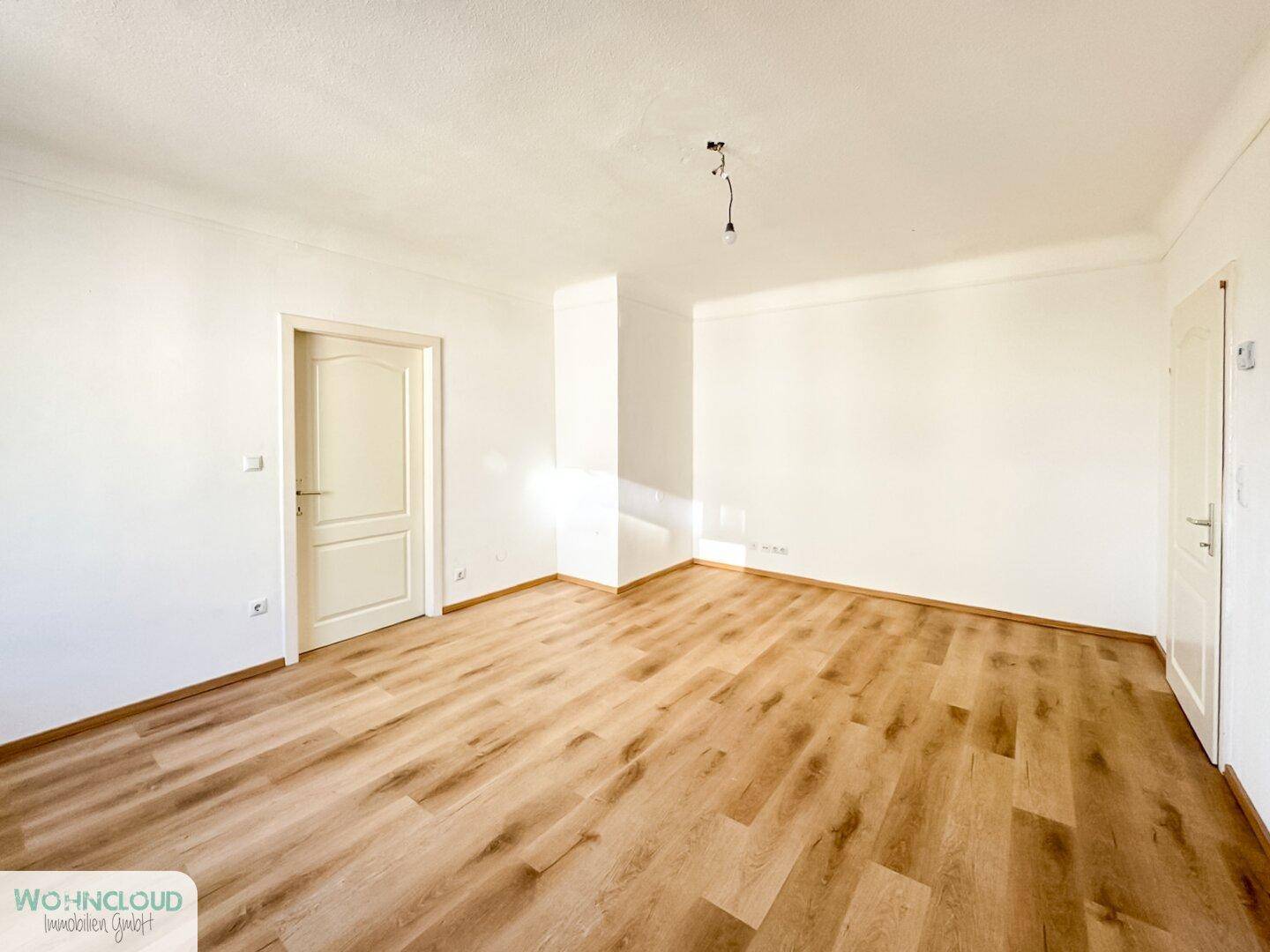 Leeres Wohnzimmer mit hellem Laminatboden und weiß gestrichenen Wänden, bereit zur Einrichtung.