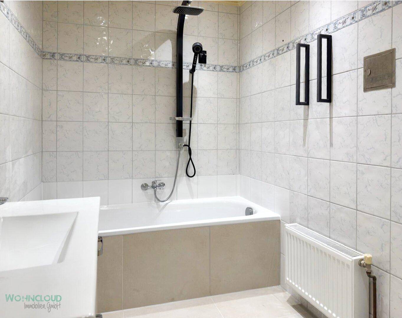 Gefliestes Badezimmer mit Badewanne, Duscharmatur und Heizkörper.
