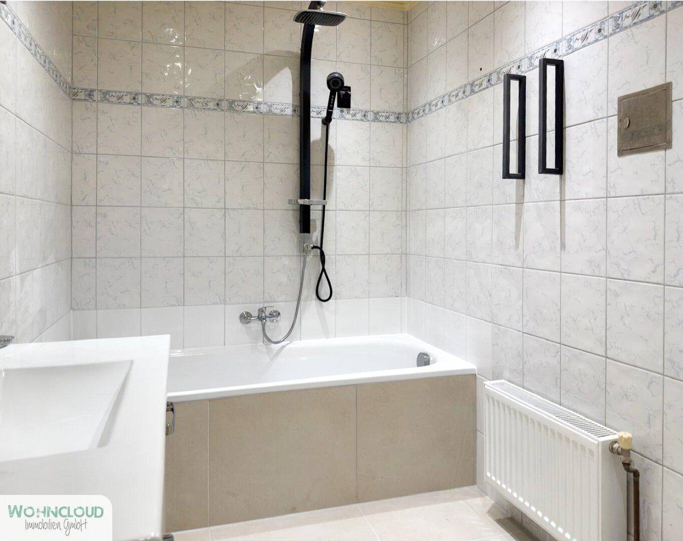 Gefliestes Badezimmer mit Badewanne, Duscharmatur und Heizkörper, in gutem Zustand.