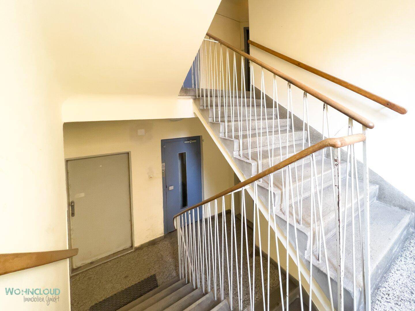 Treppenhaus mit Steinstufen und Metallgeländer in einem Mehrfamilienhaus.