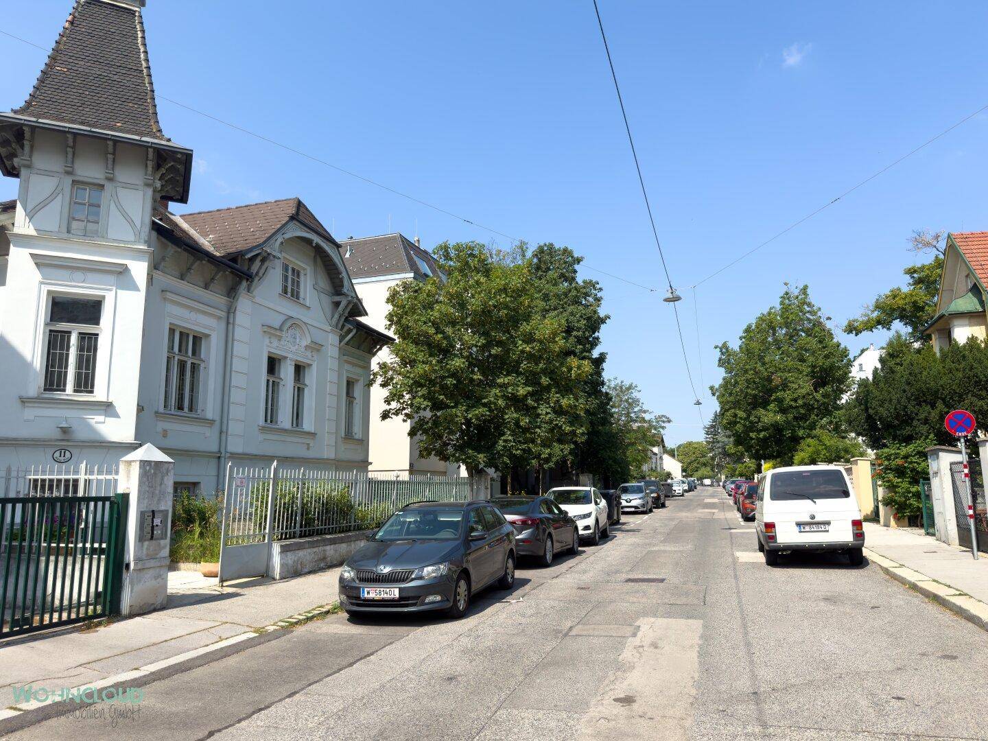 Ruhige Wohnstraße mit parkenden Autos und historischen Gebäuden unter blauem Himmel.