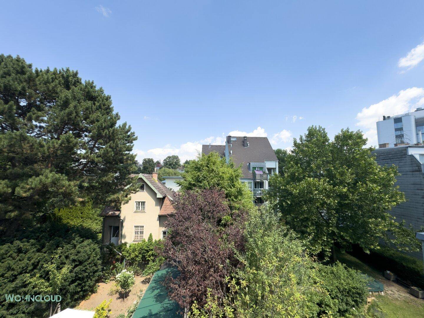 Weitläufiger Blick ins Grüne mit Bäumen und umliegenden Häusern unter blauem Himmel.
