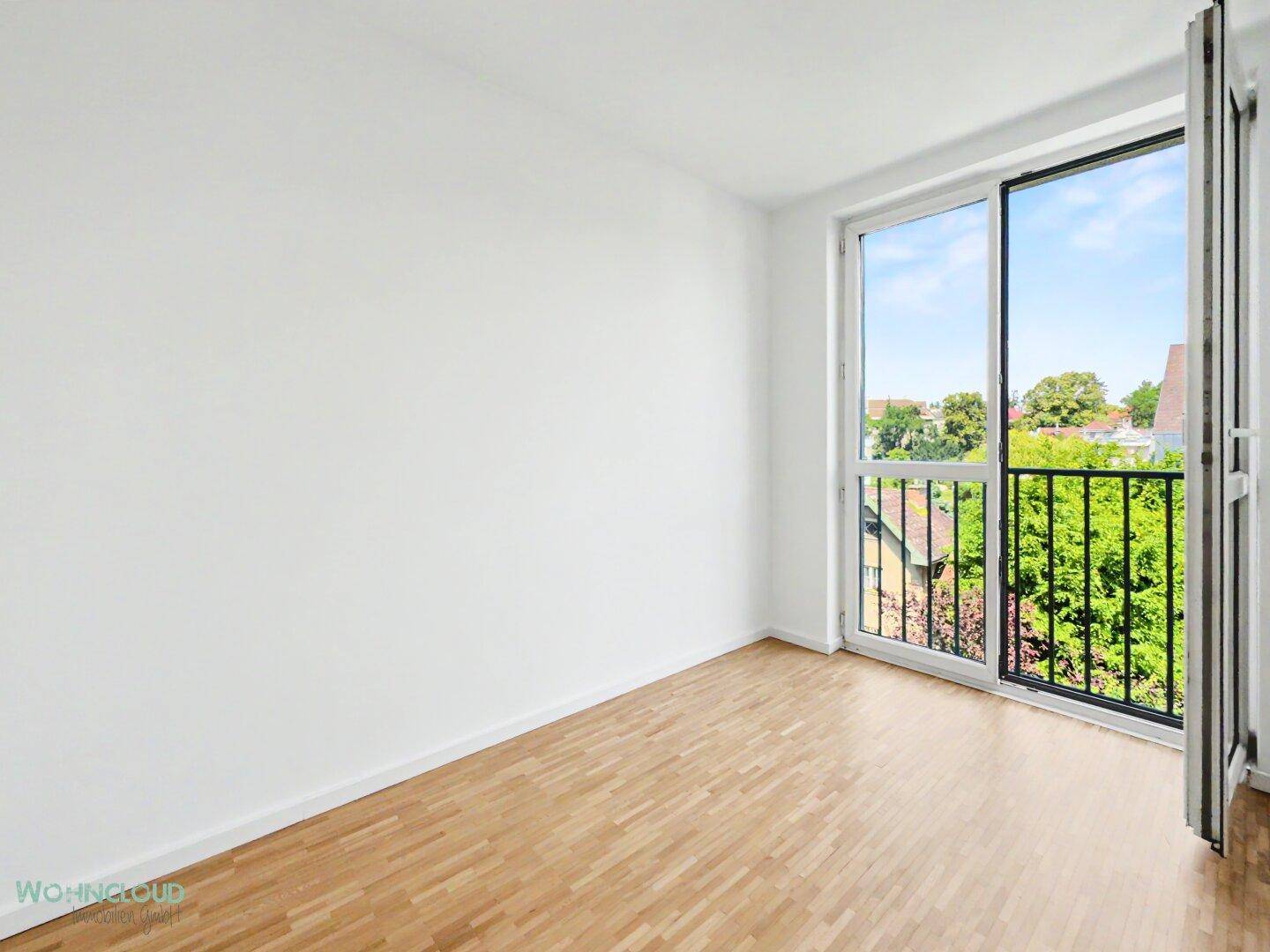 Helles Zimmer mit Parkettboden und einem französischen Balkon mit Blick ins Grüne.